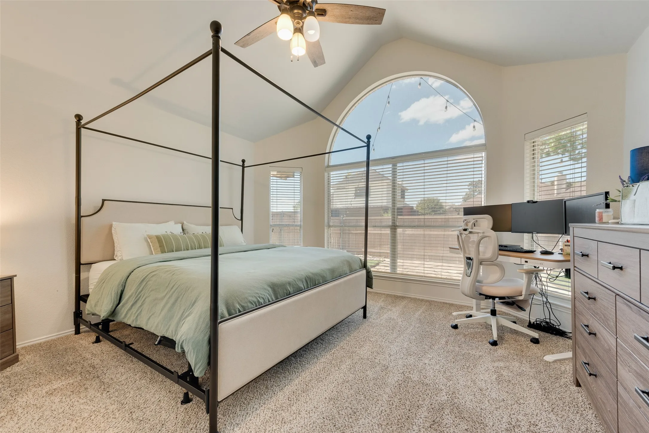 Arched window with blinds, vaulted ceiling, ceiling fan, and carpeted flooring