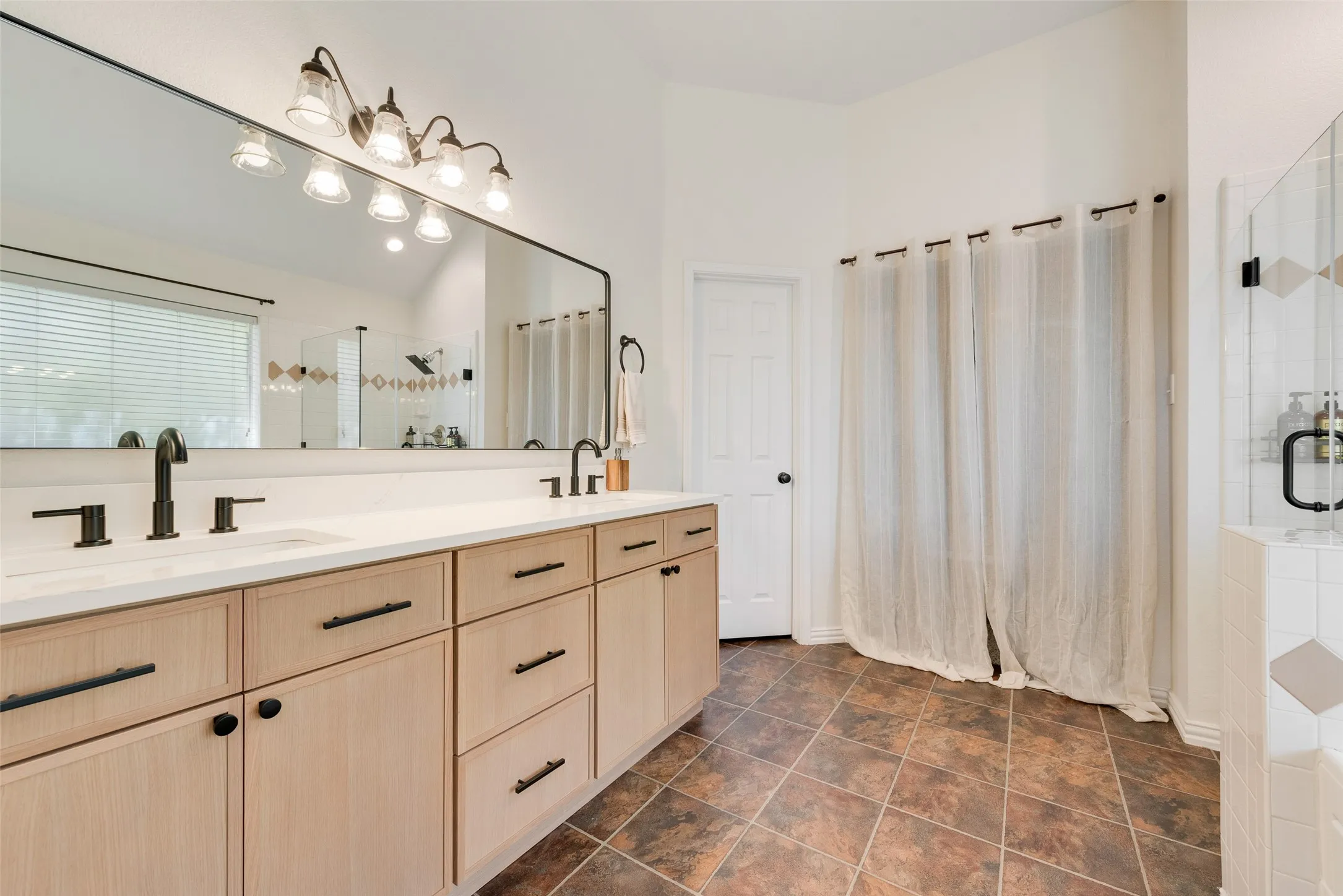 Dual vanity with integrated sinks, light wood-finish cabinetry, and black hardware