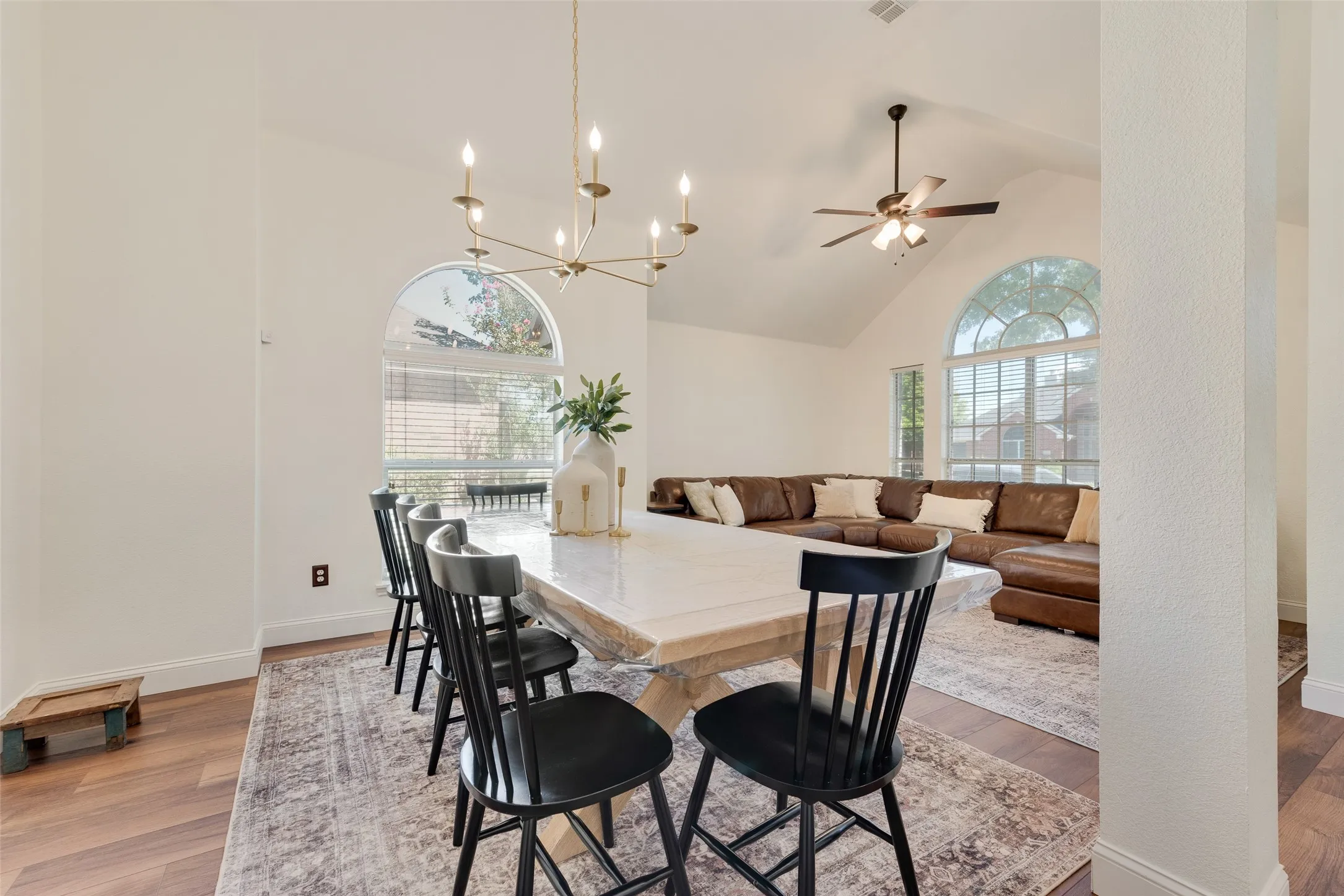 Vaulted ceilings with a ceiling fan, arched windows, and a multi-arm brass chandelier