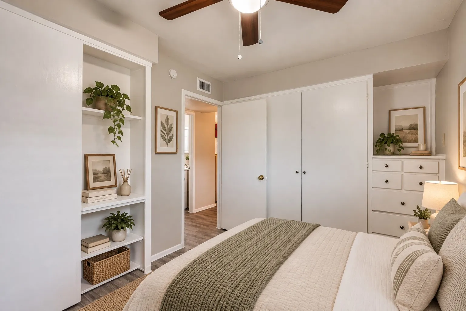 Recessed built-in shelving, wood-finish flooring, white paneled closet doors, built-in dresser, and a ceiling fan with integrated lighting