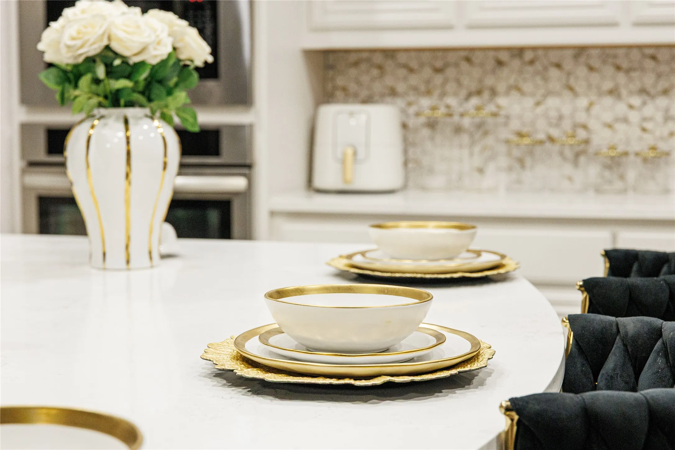 White countertop with a curved edge, stainless steel built-in ovens, and a patterned backsplash