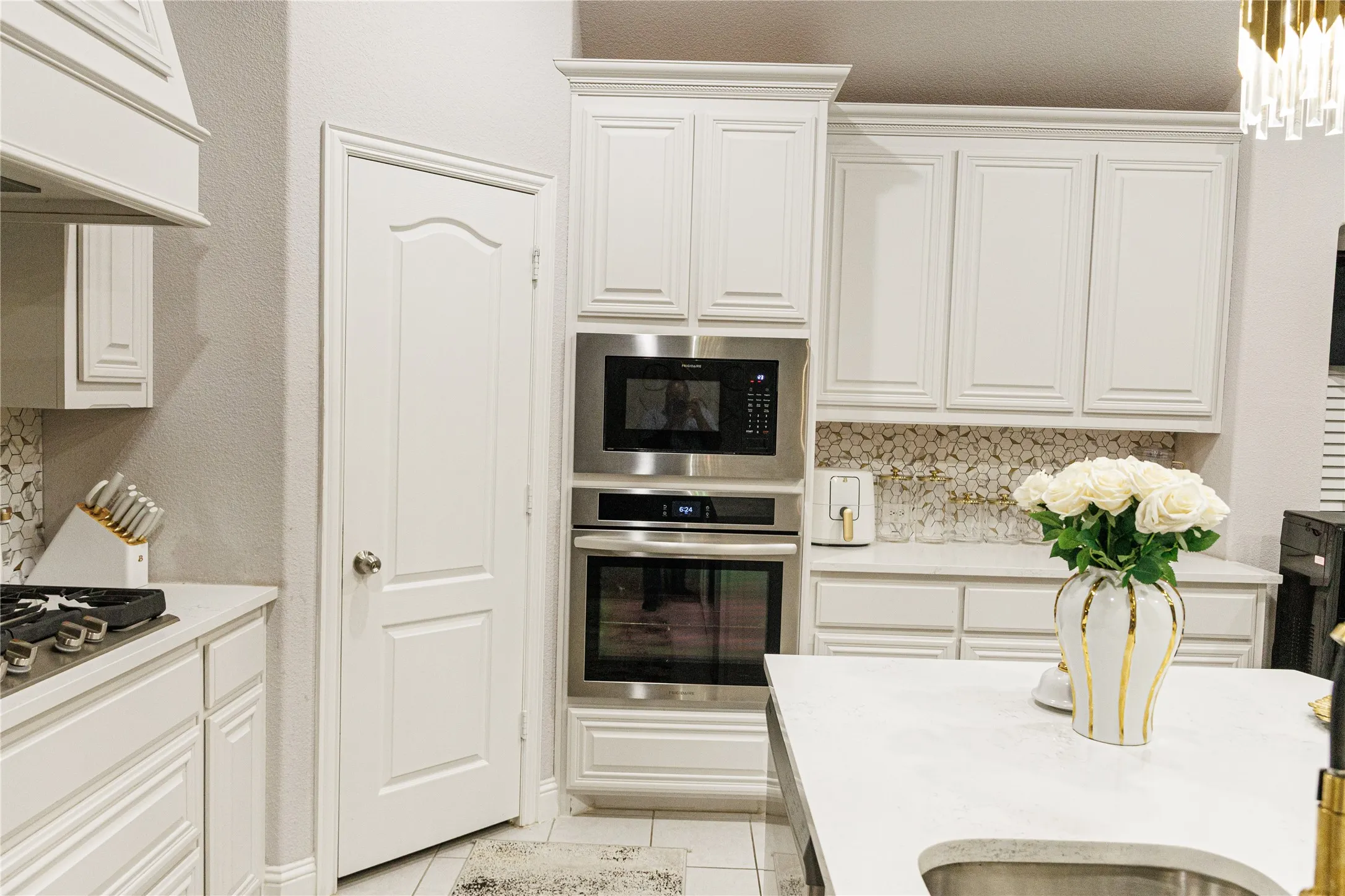 White cabinetry with crown molding, stainless steel built-in appliances, a tiled backsplash, and a light-toned countertop
