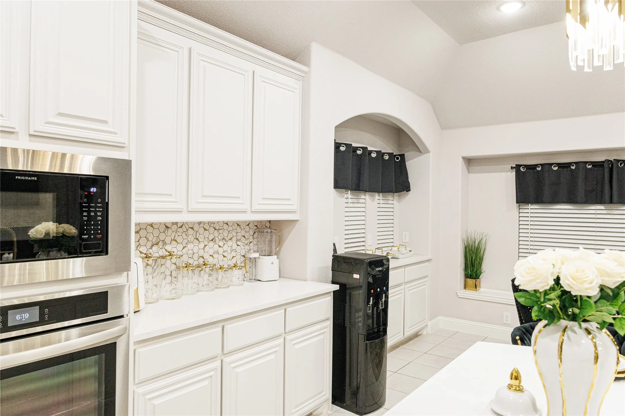 Recessed lighting, vaulted ceiling, built-in stainless steel microwave and oven, white cabinetry, and honeycomb tile backsplash