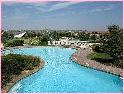 Curved swimming pool with integrated steps, surrounded by a paved deck and lounge seating
