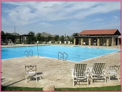 Expansive outdoor swimming pool with concrete decking, featuring a stone-clad cabana with a red tile roof and an additional covered pergola area