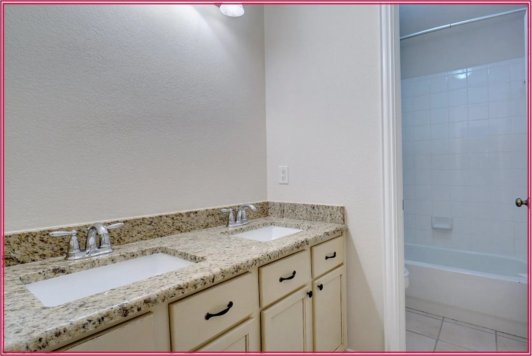 Dual vanity with granite-style countertop, undermount sinks, chrome fixtures, and cream-colored cabinetry