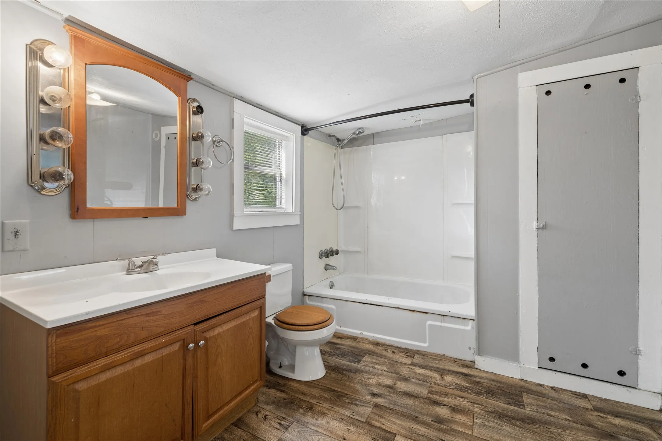 Wood-finish flooring, vanity with wood-finish cabinetry, integrated sink, and a combination bathtub and shower