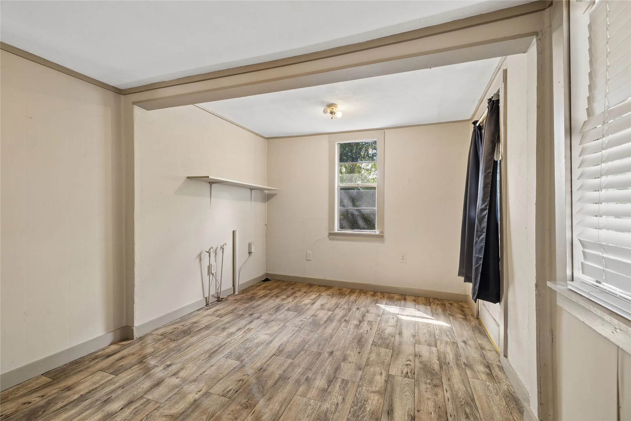 Wood-finish flooring throughout, with a window featuring blinds, and a built-in shelf
