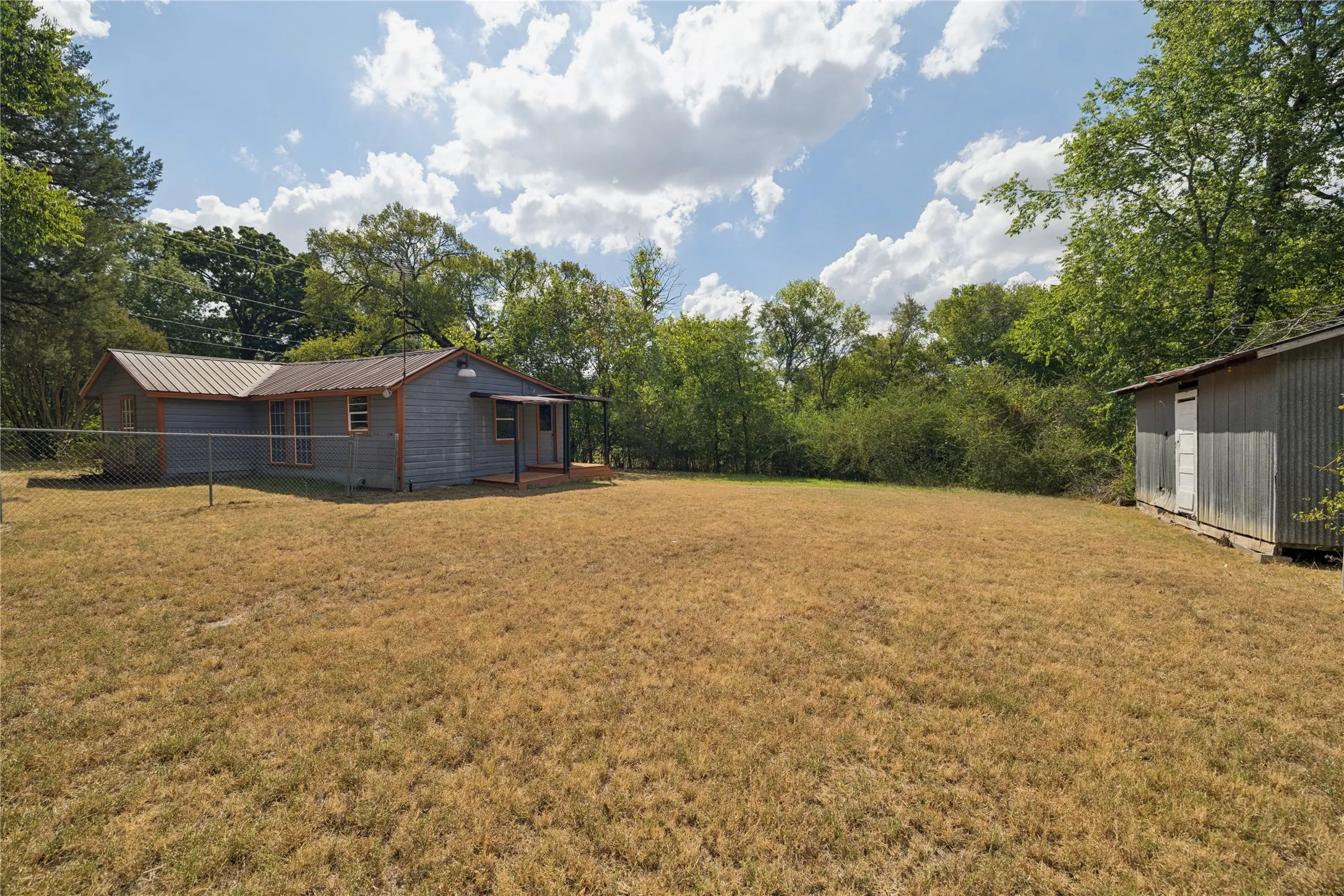 Metal roof residence featuring a covered porch, chain-link fencing, and a separate storage shed