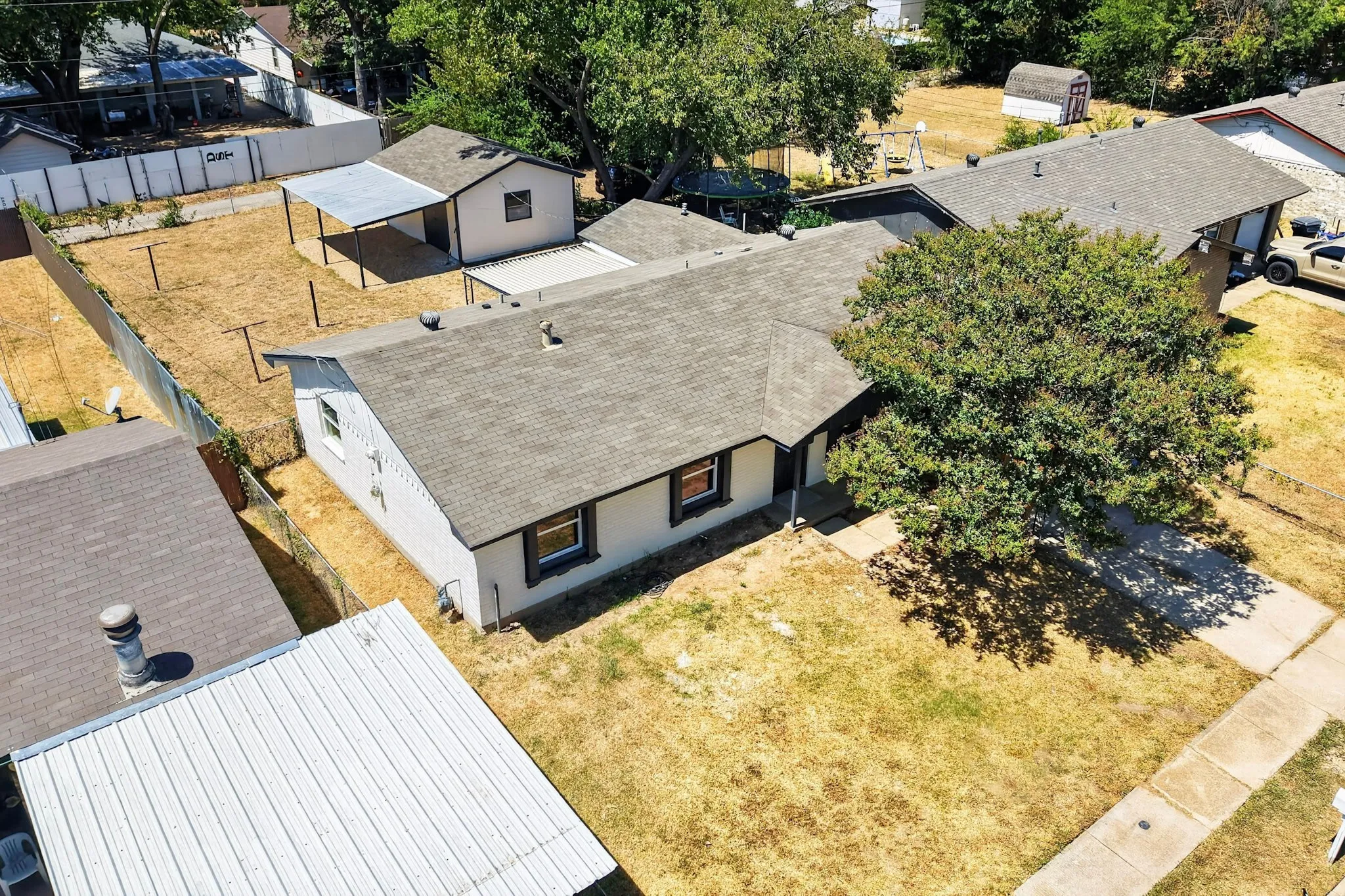 Property featuring a gabled roof, mature front yard tree, concrete sidewalk, fenced backyard, and a detached shed with an attached carport