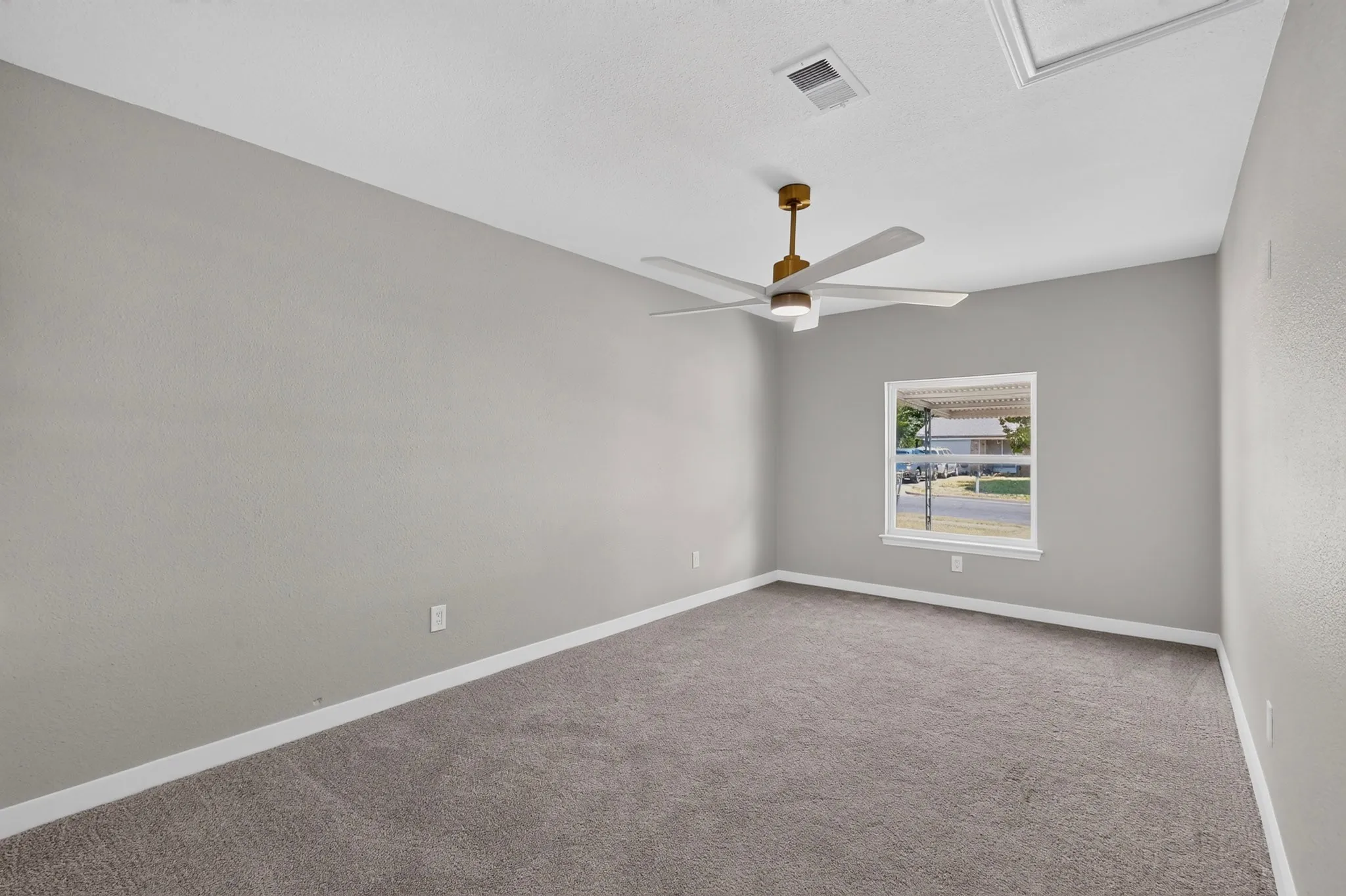 Spacious room featuring gray textured walls, gray carpet flooring, a single window, and a ceiling fan with integrated lighting