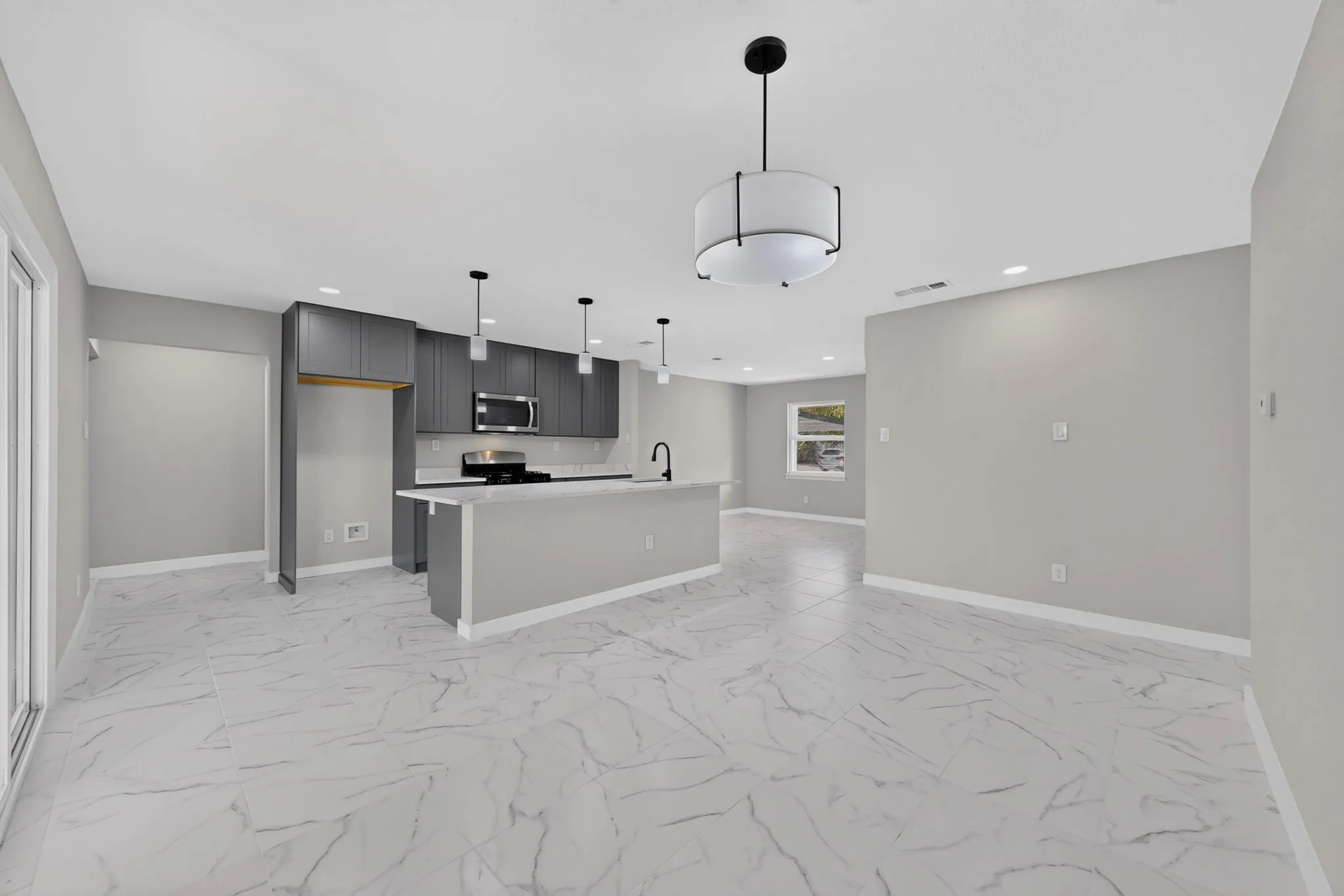 Spacious open-concept layout featuring marble-look floor tile, a kitchen island with seating, stainless steel appliances, and contemporary pendant lighting