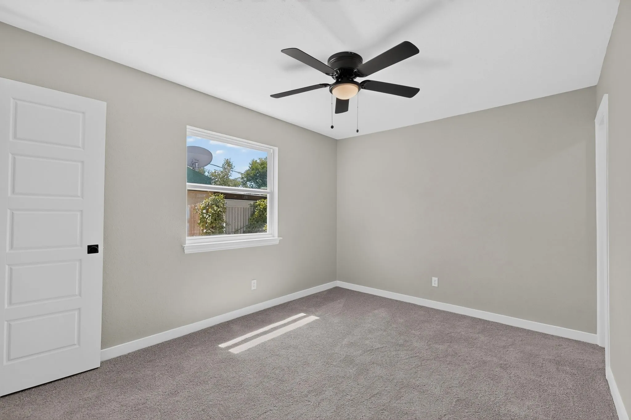 Neutral wall paint, gray carpeting, white trim, white paneled door with dark hardware, and a ceiling fan with integrated lighting