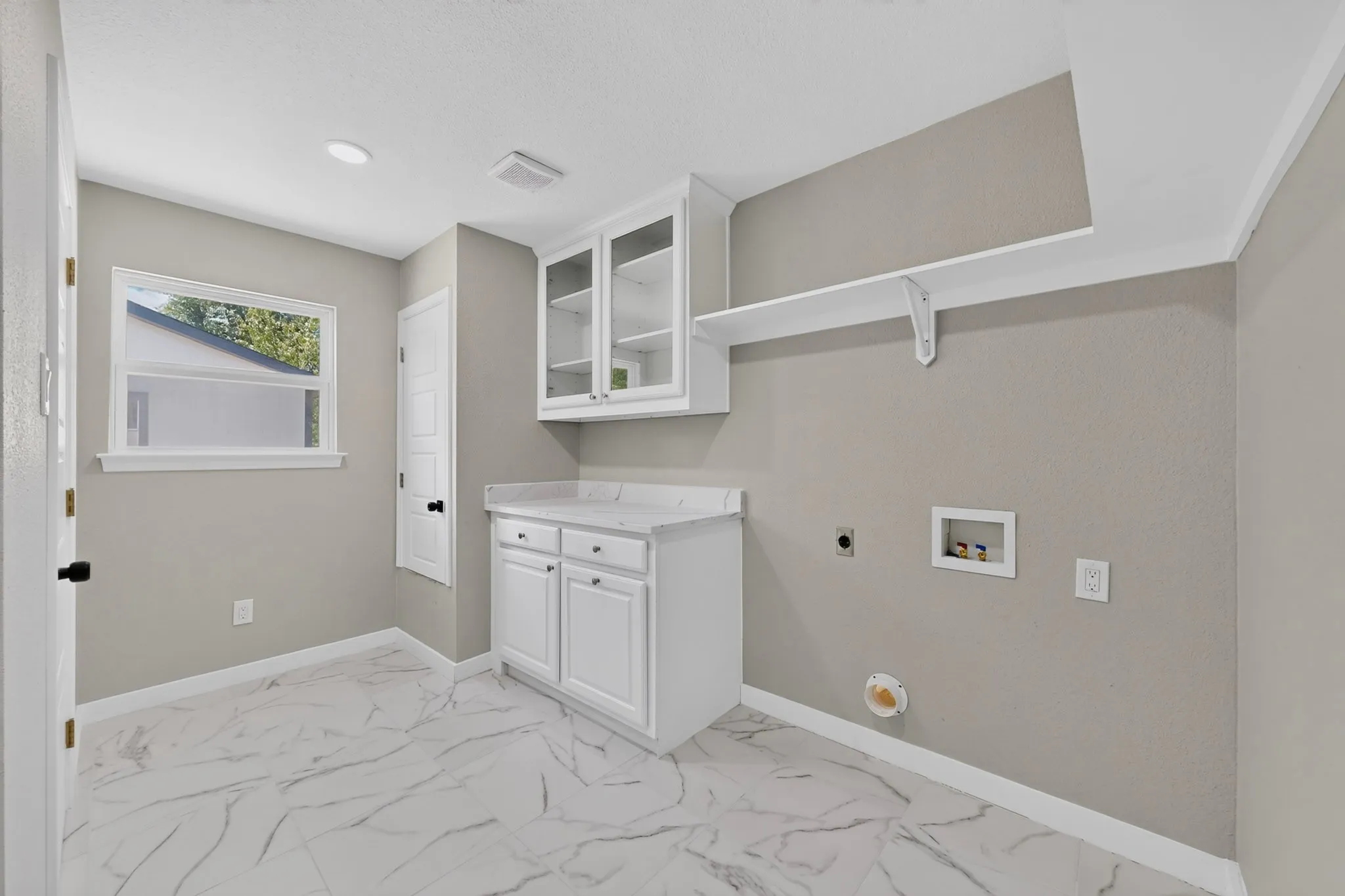 White cabinetry with glass-front upper cabinets, light-toned countertop, and patterned floor tile
