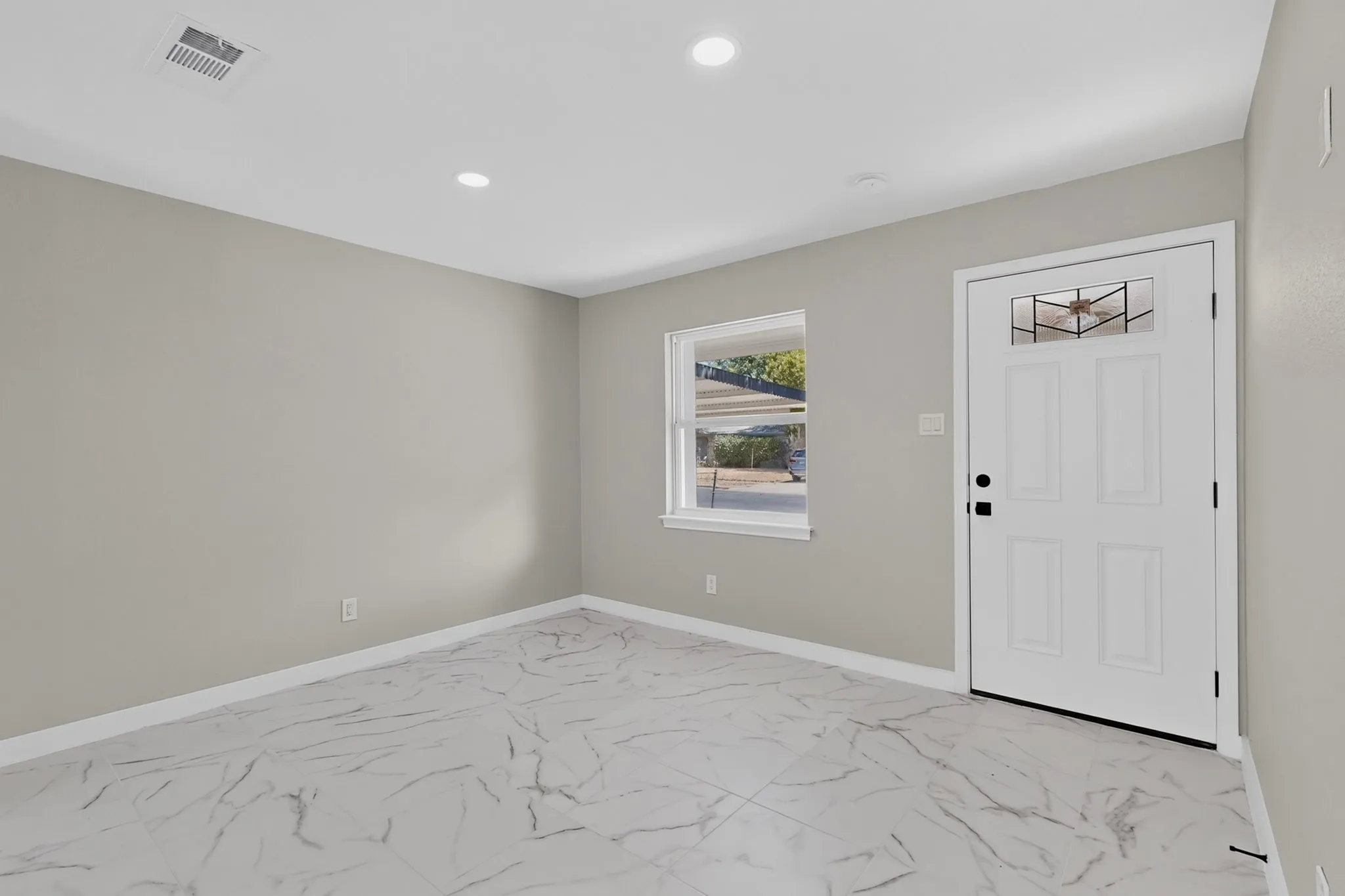 Recessed lighting, white trim, light gray walls, white panel door with decorative glass inlay, and marble-look tile flooring