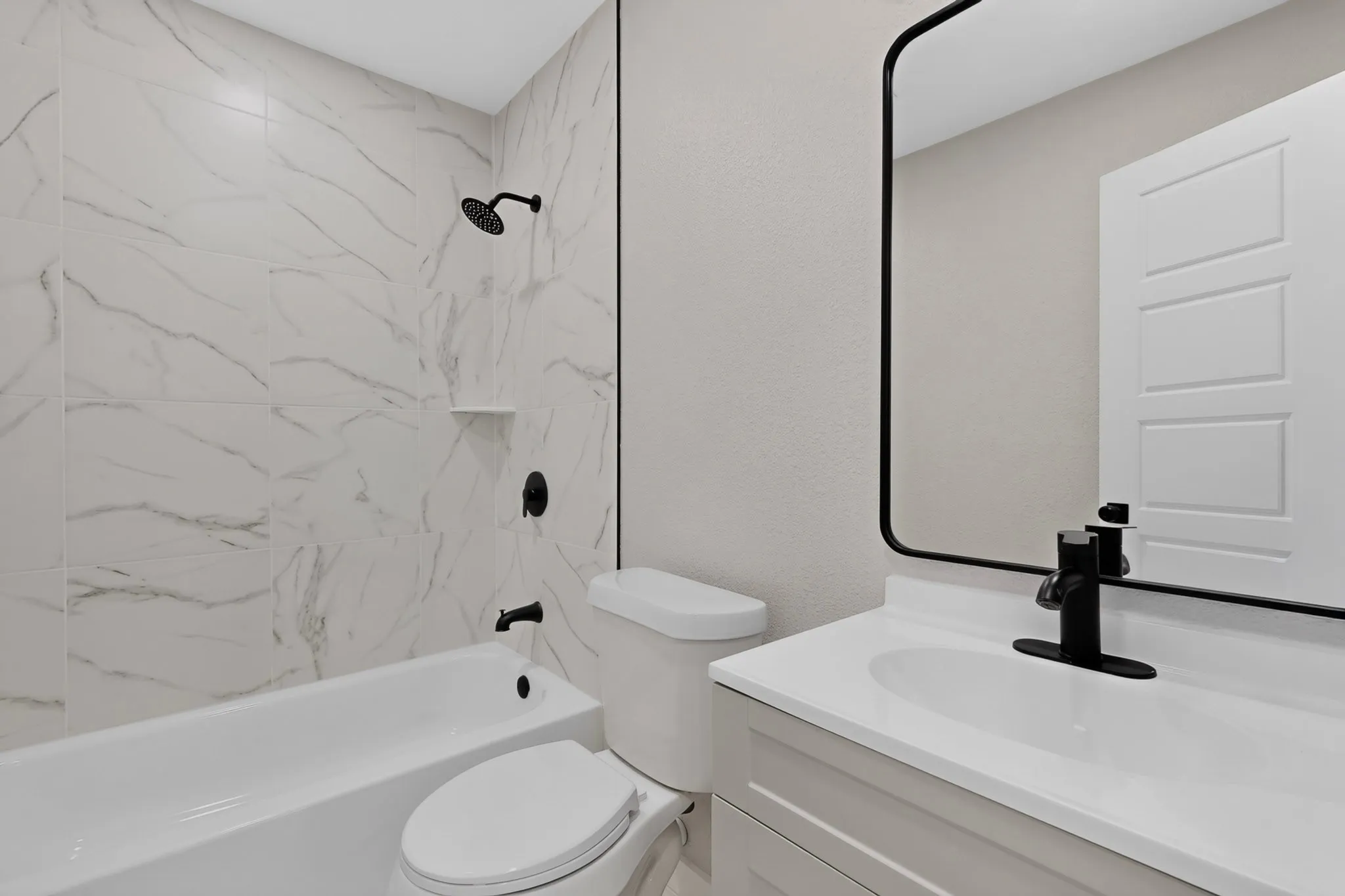 White bath and shower combination with black fixtures, vanity with integrated sink, and framed mirror