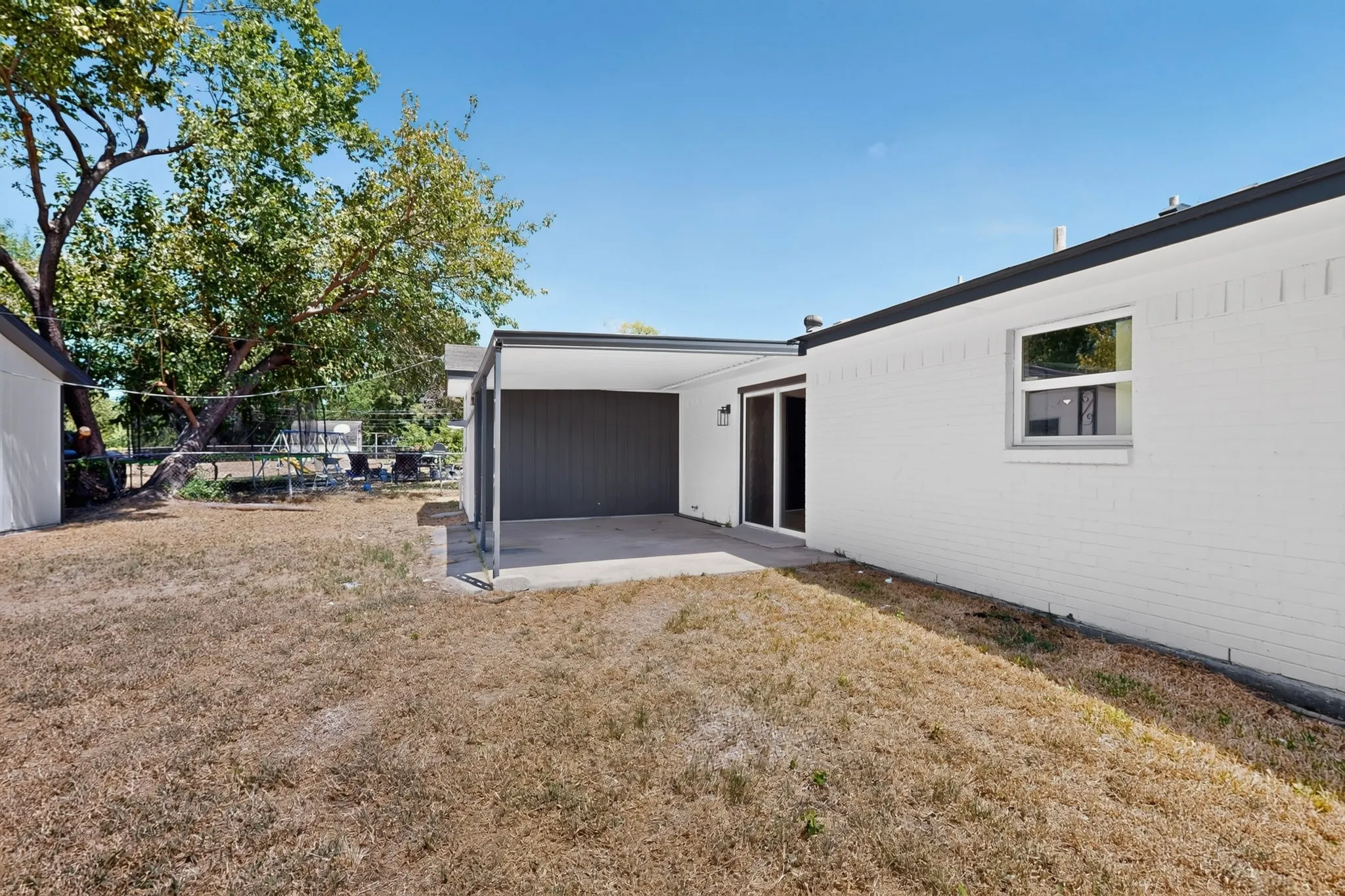 Expansive backyard featuring a covered patio with concrete flooring, white painted brick exterior, and a sliding glass door