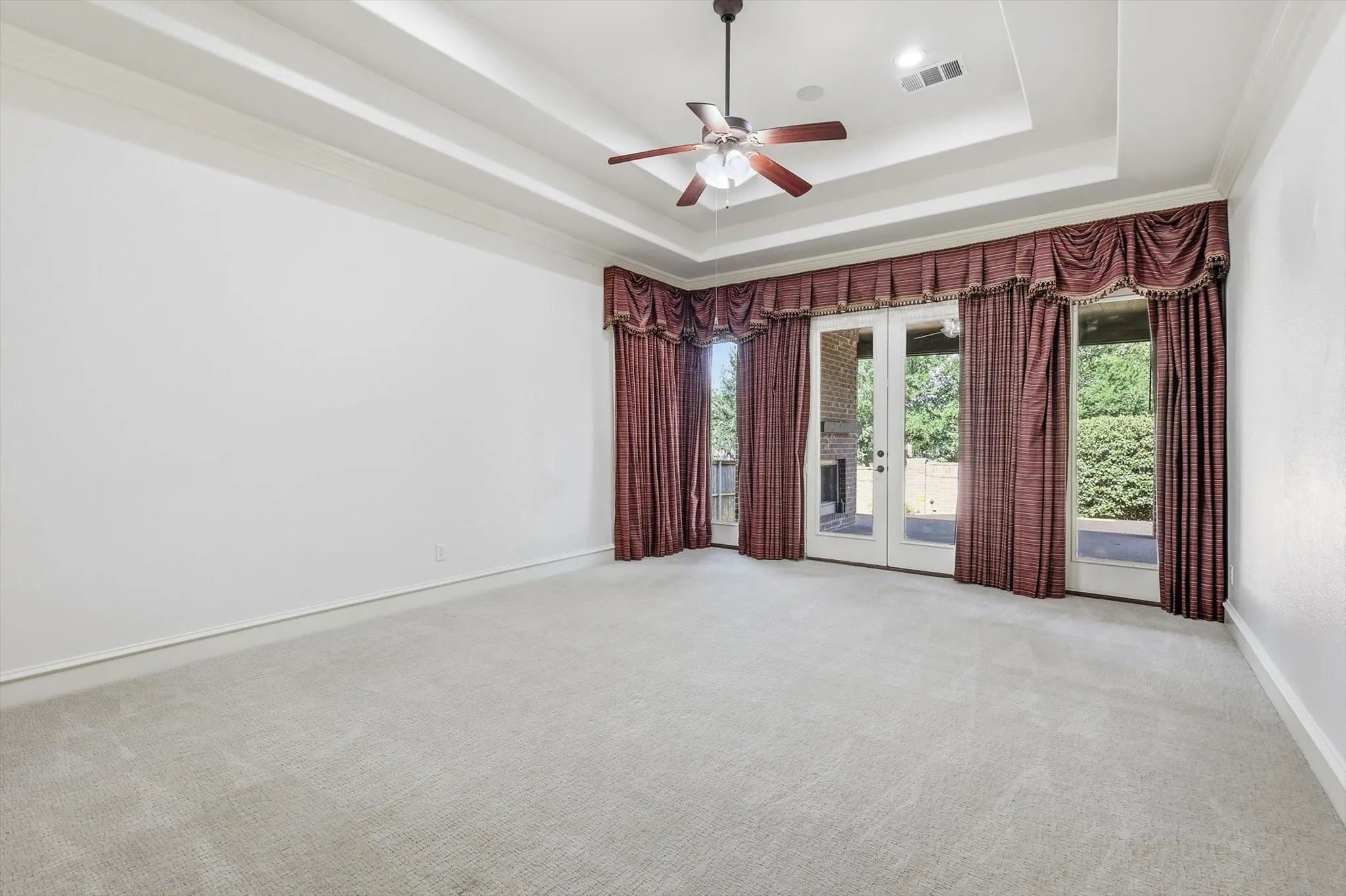 Tray ceiling with crown molding, ceiling fan, recessed lighting, and double glass doors