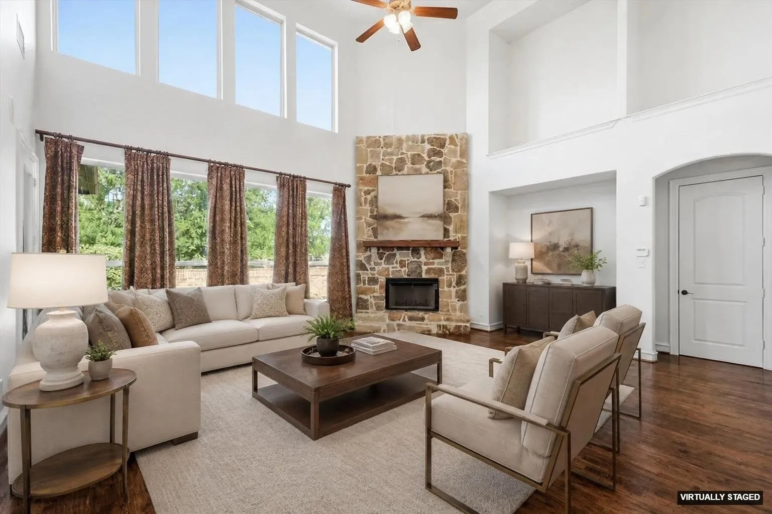 Two-story living area featuring a stacked stone fireplace with a wood-finish mantel, dark wood-finish flooring, and high ceilings with upper windows