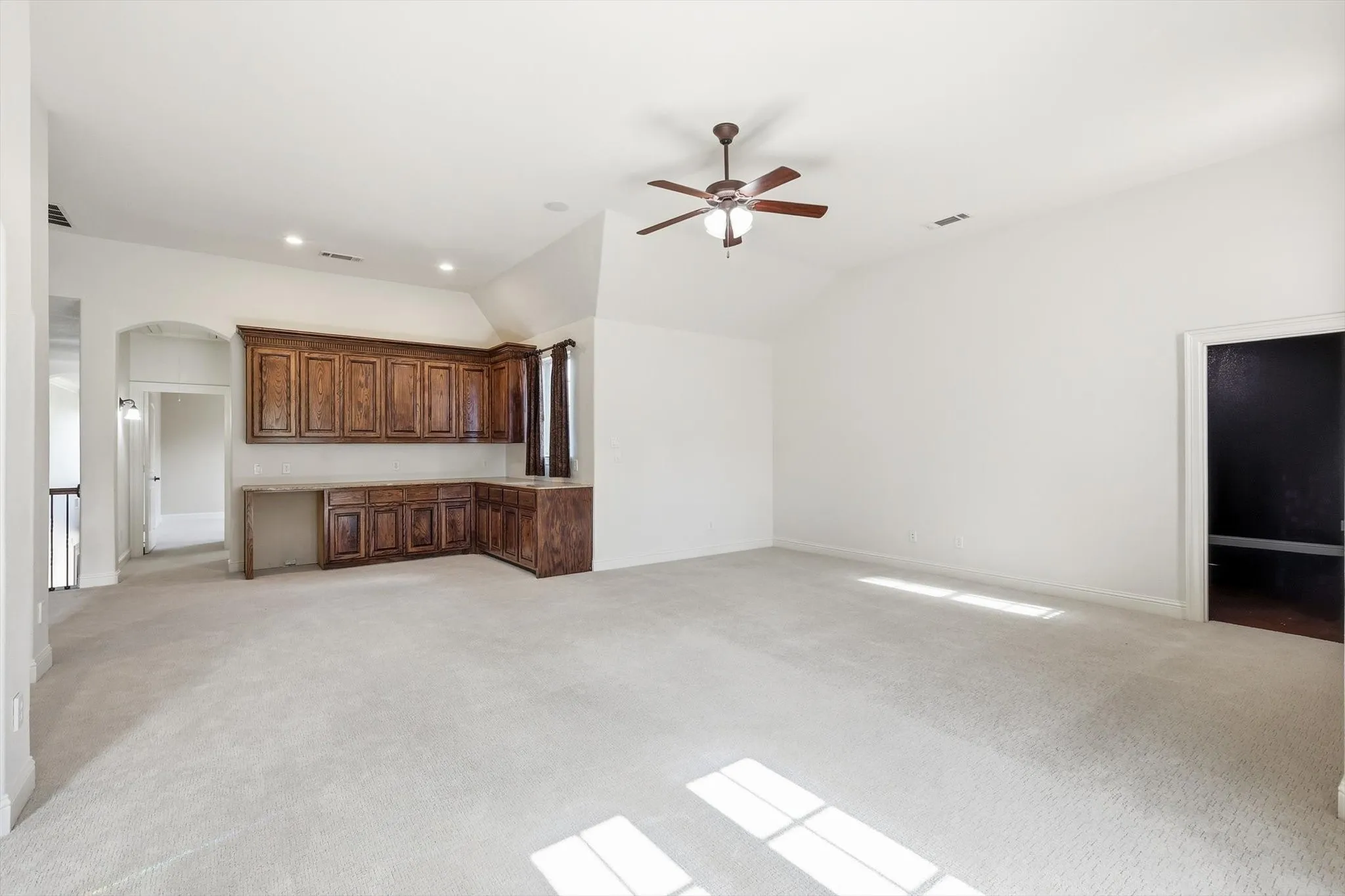 Vaulted ceiling with a ceiling fan, recessed lighting, built-in wood cabinetry, light-toned carpeting, and an arched entryway