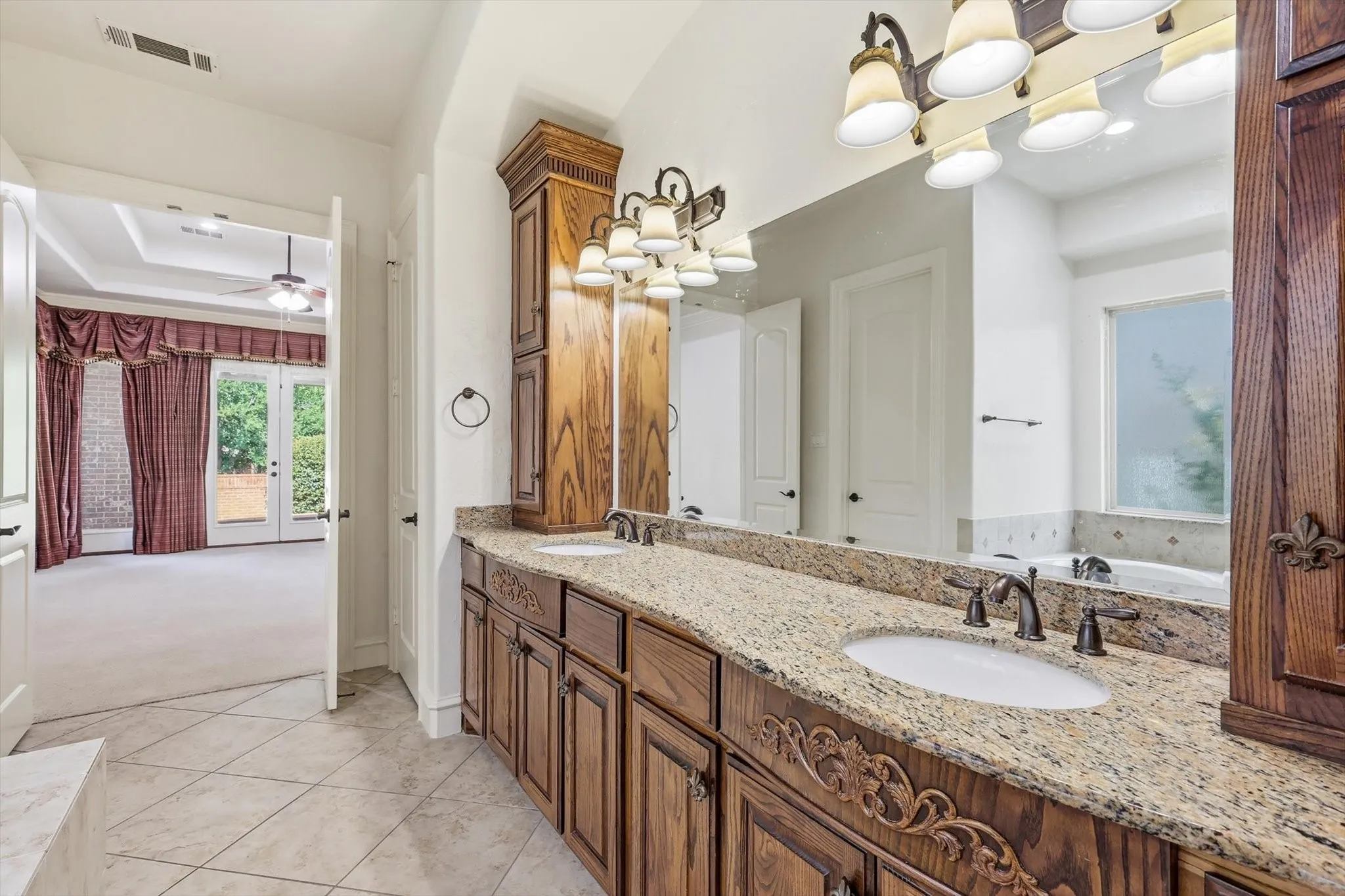 Dual vanity with stone countertop, ornate wood cabinetry, and oil-rubbed bronze fixtures