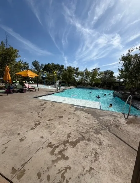 Expansive swimming pool featuring a concrete deck and lush surrounding trees