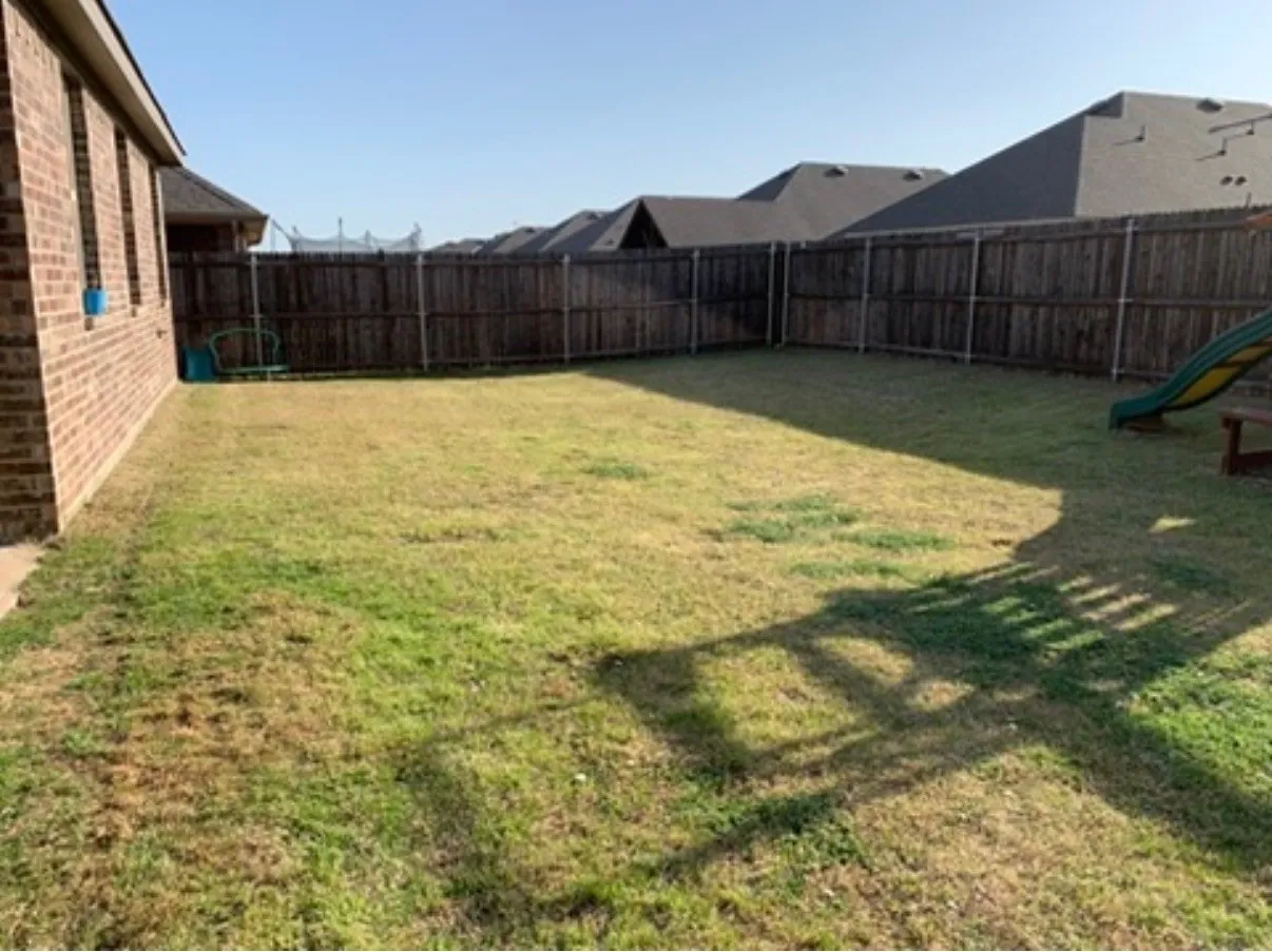 Expansive backyard featuring a full privacy fence and a brick exterior