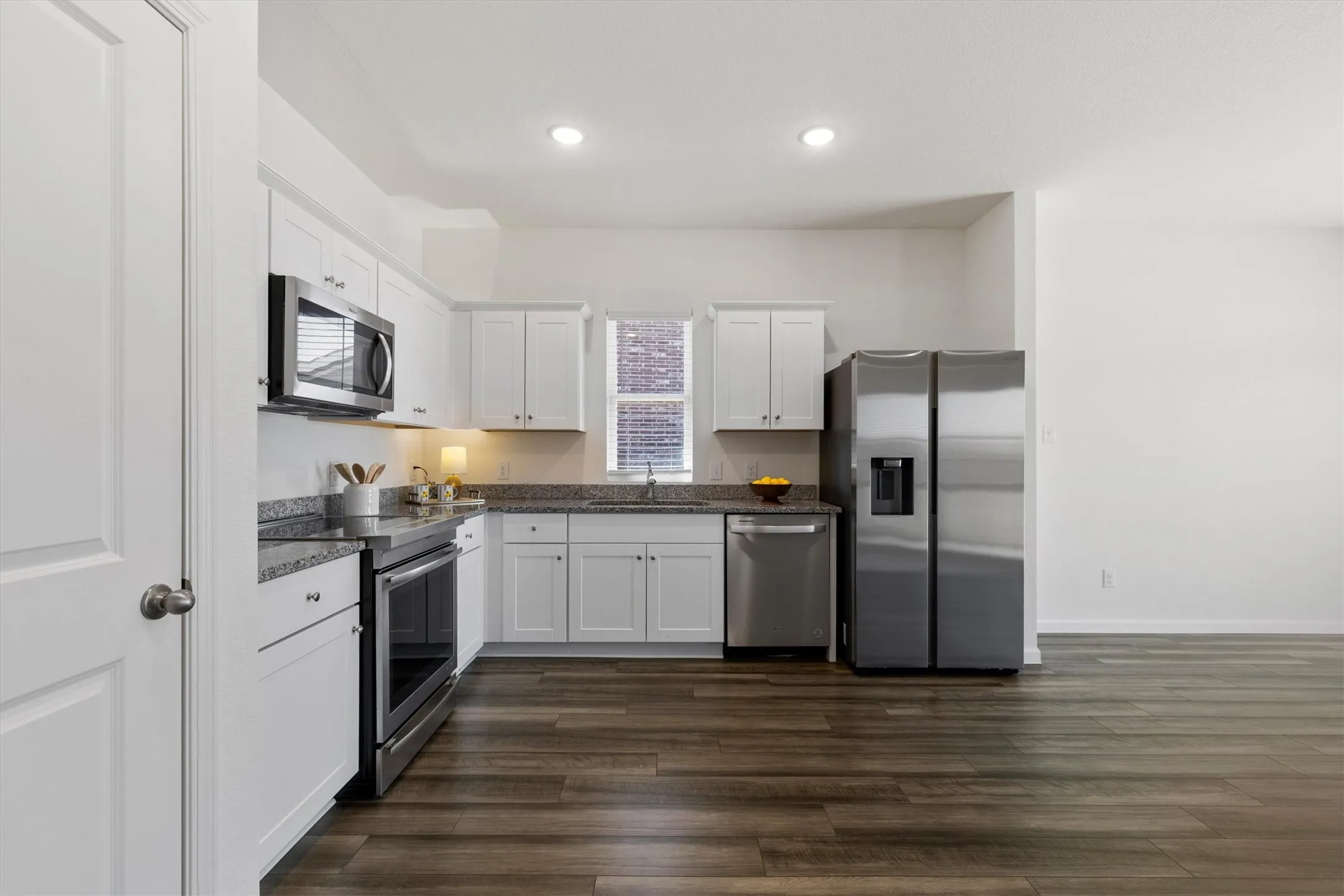Kitchen featuring white cabinetry, stainless steel appliances, granite like countertops, and wood-finish flooring