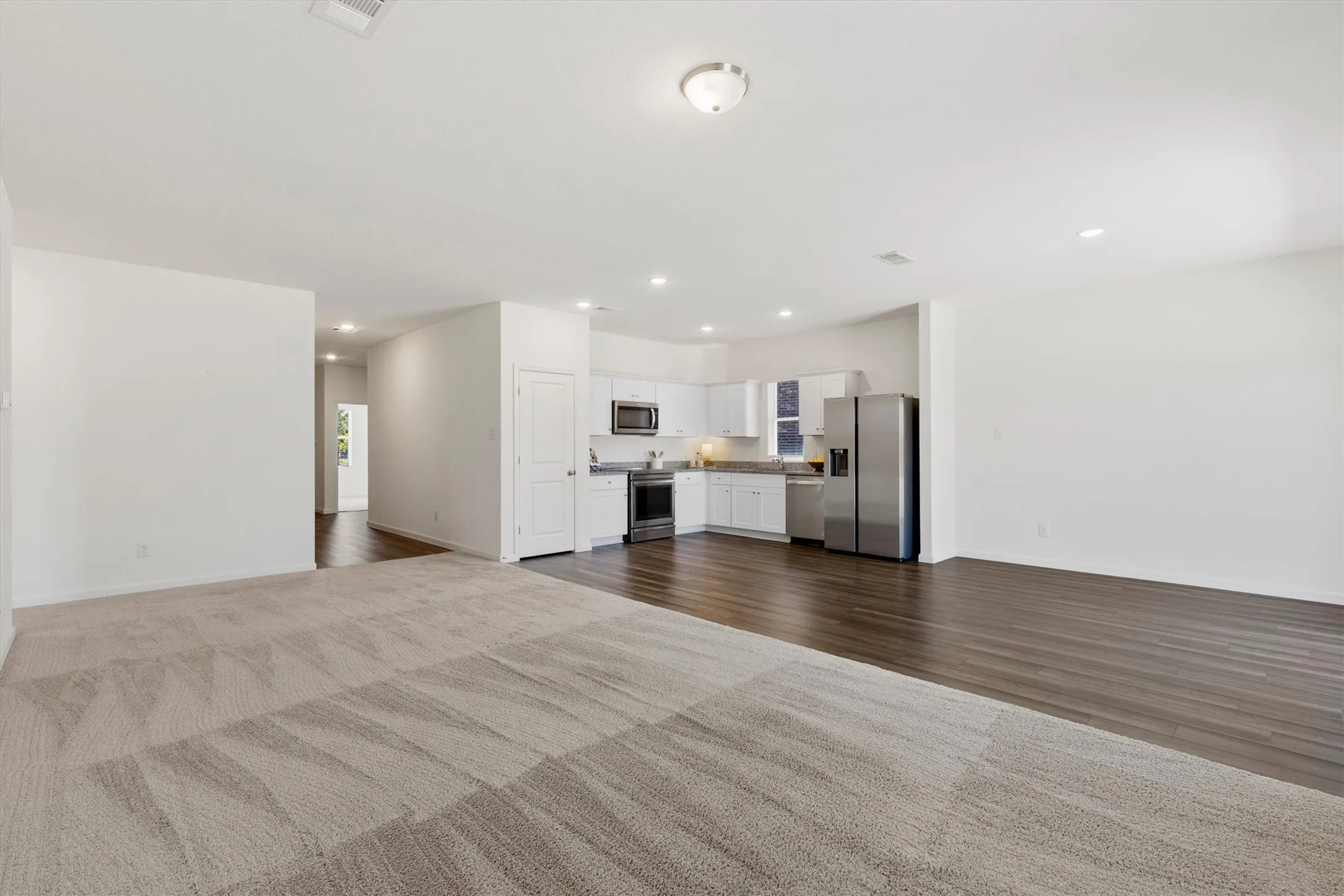 Open-concept living space featuring carpet, wood look laminate flooring, recessed lighting, and a kitchen with white cabinetry and stainless steel appliances