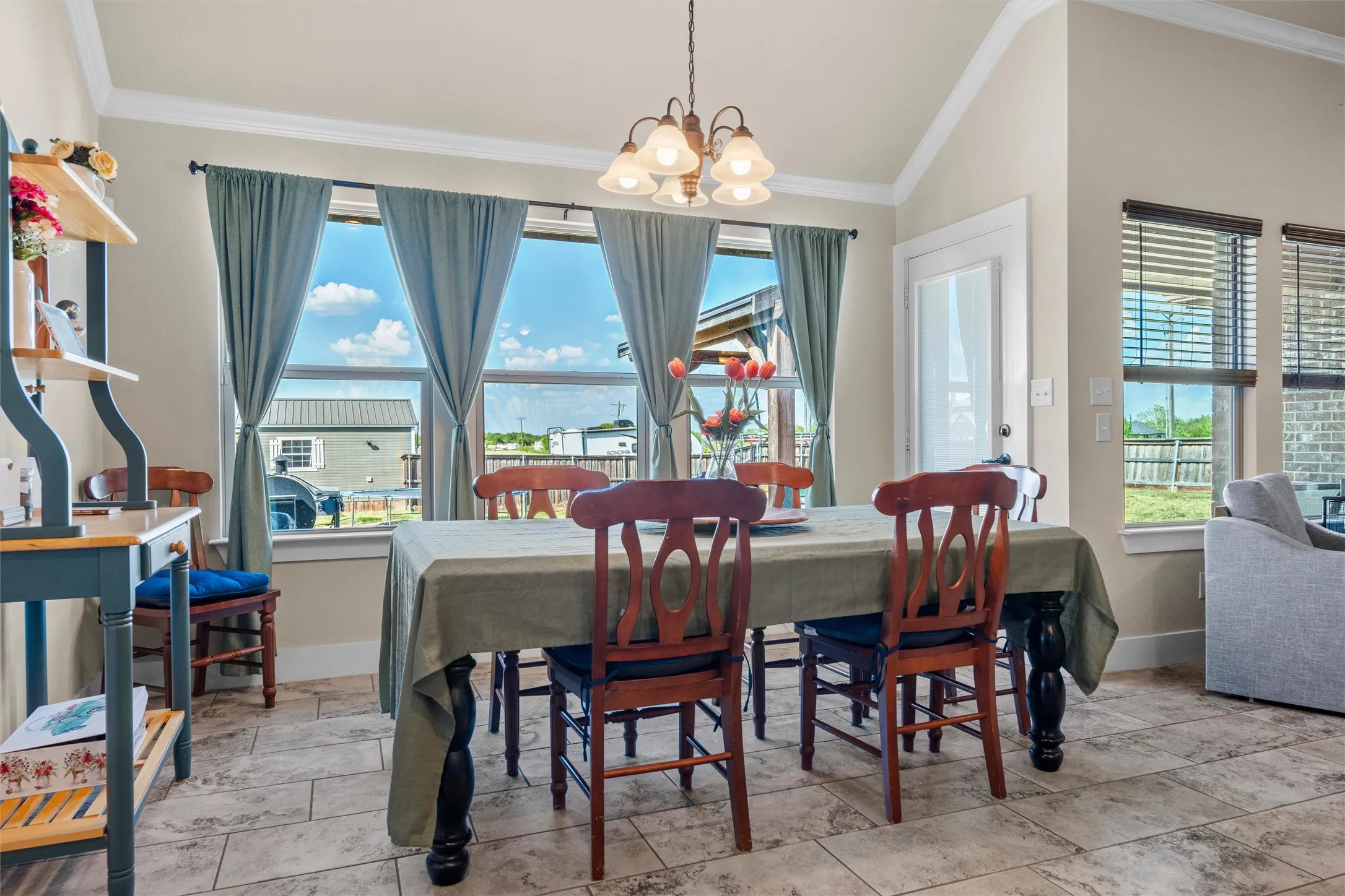 Vaulted ceiling with crown molding, three large windows, tiled flooring, and a chandelier-style light fixture