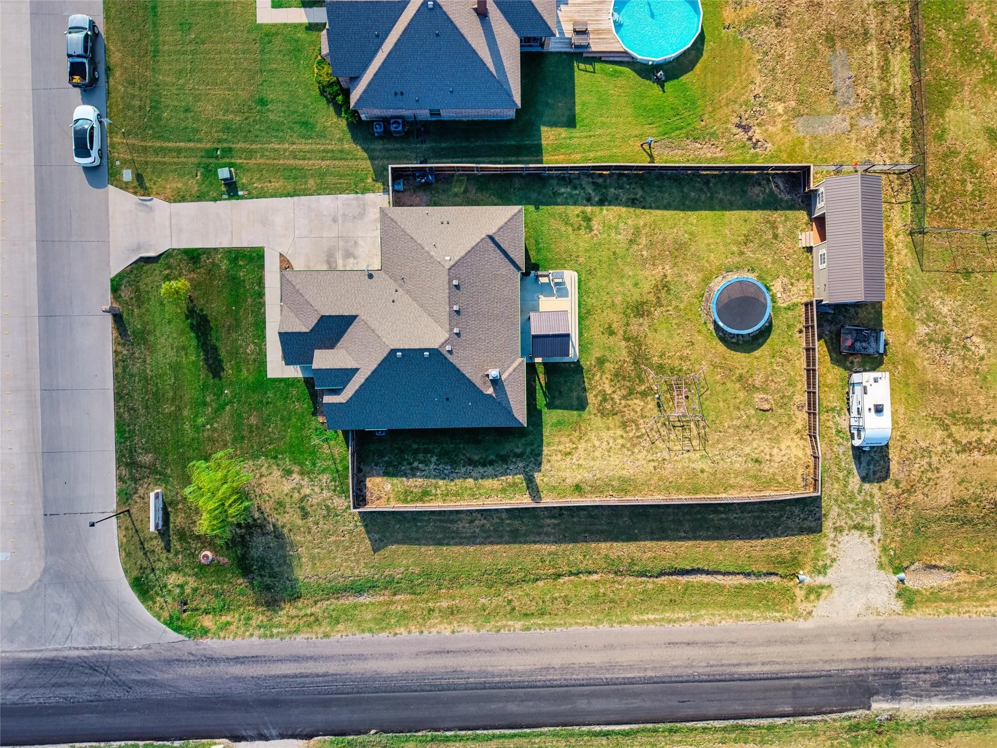 Expansive property featuring a paved driveway, a structure with a dark shingle roof, a fenced backyard, and a detached shed