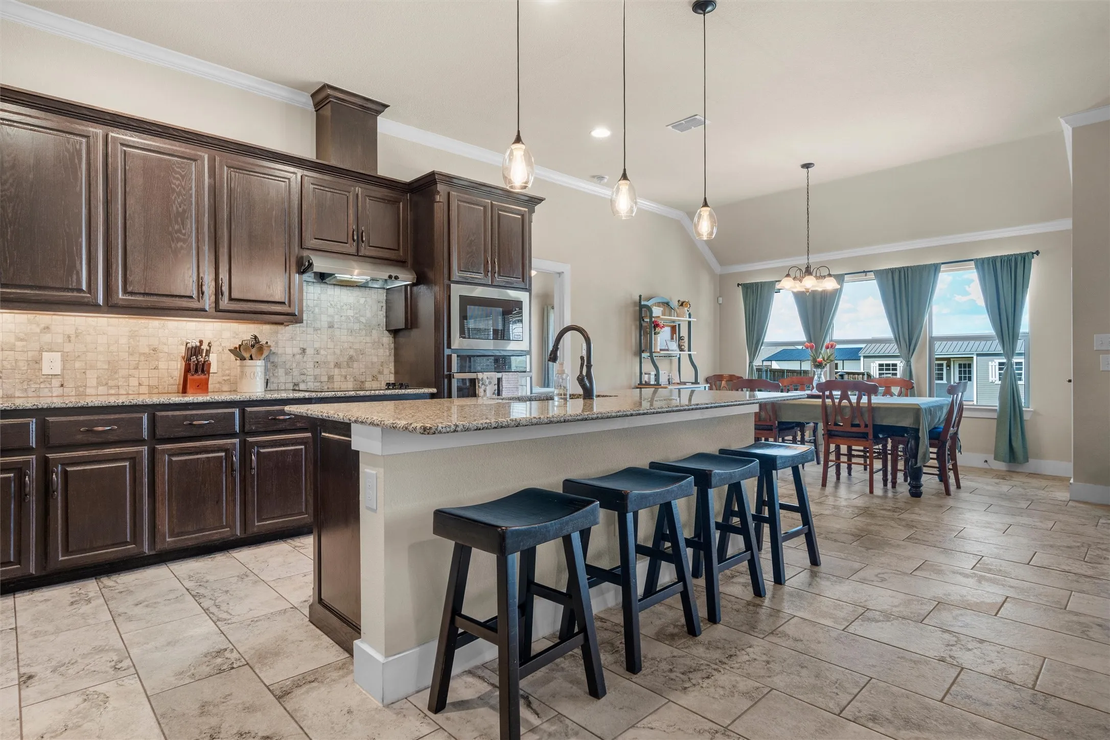 Expansive kitchen featuring dark wood cabinetry, a mosaic tile backsplash, built-in stainless steel appliances, and a central island with a granite-style countertop
