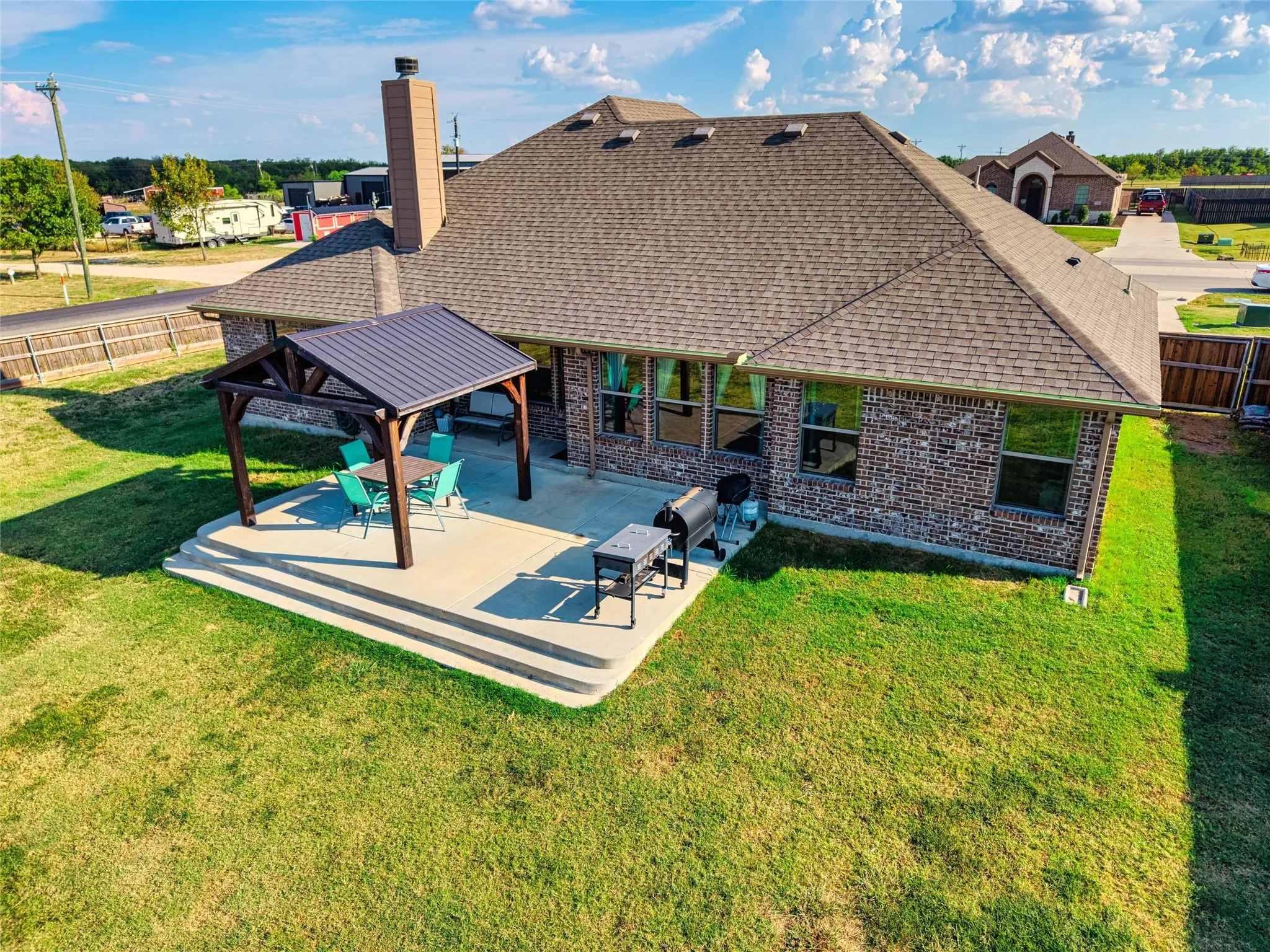 Brick exterior with a prominent chimney, a covered patio featuring a metal roof, and a tiered concrete patio