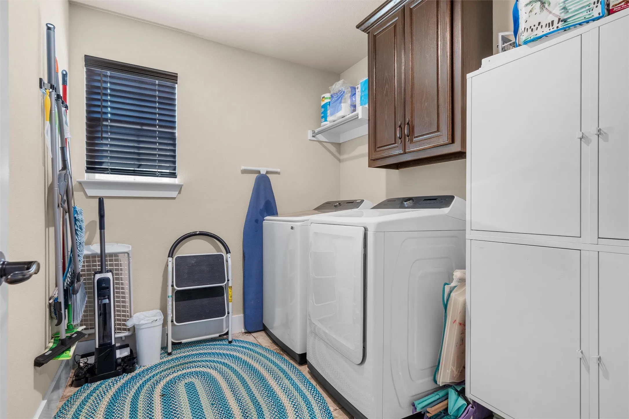 Laundry area featuring upper cabinetry, white shelving, and a window with blinds
