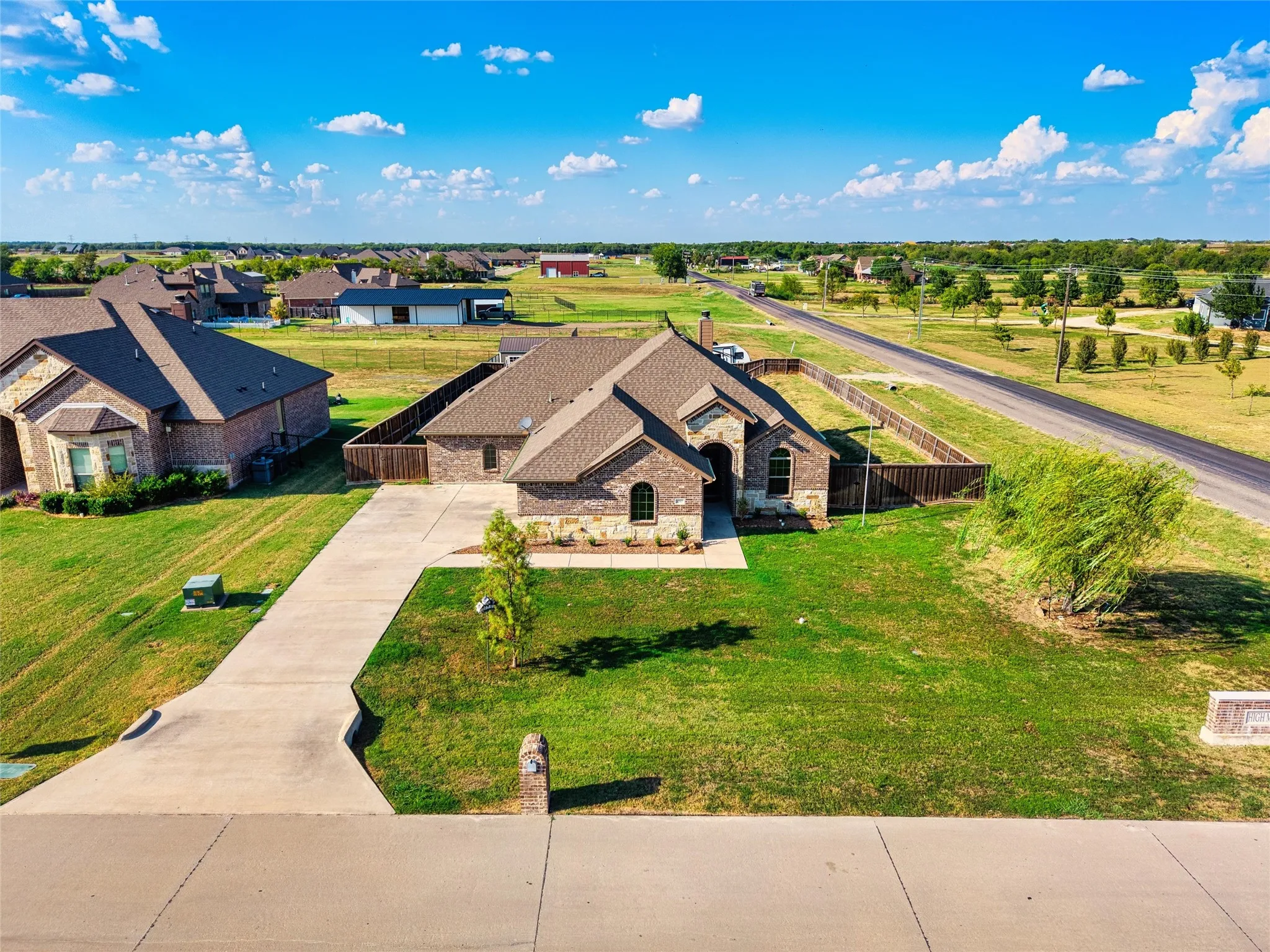 Brick and stone exterior, concrete driveway, fenced yard, and mature landscaping