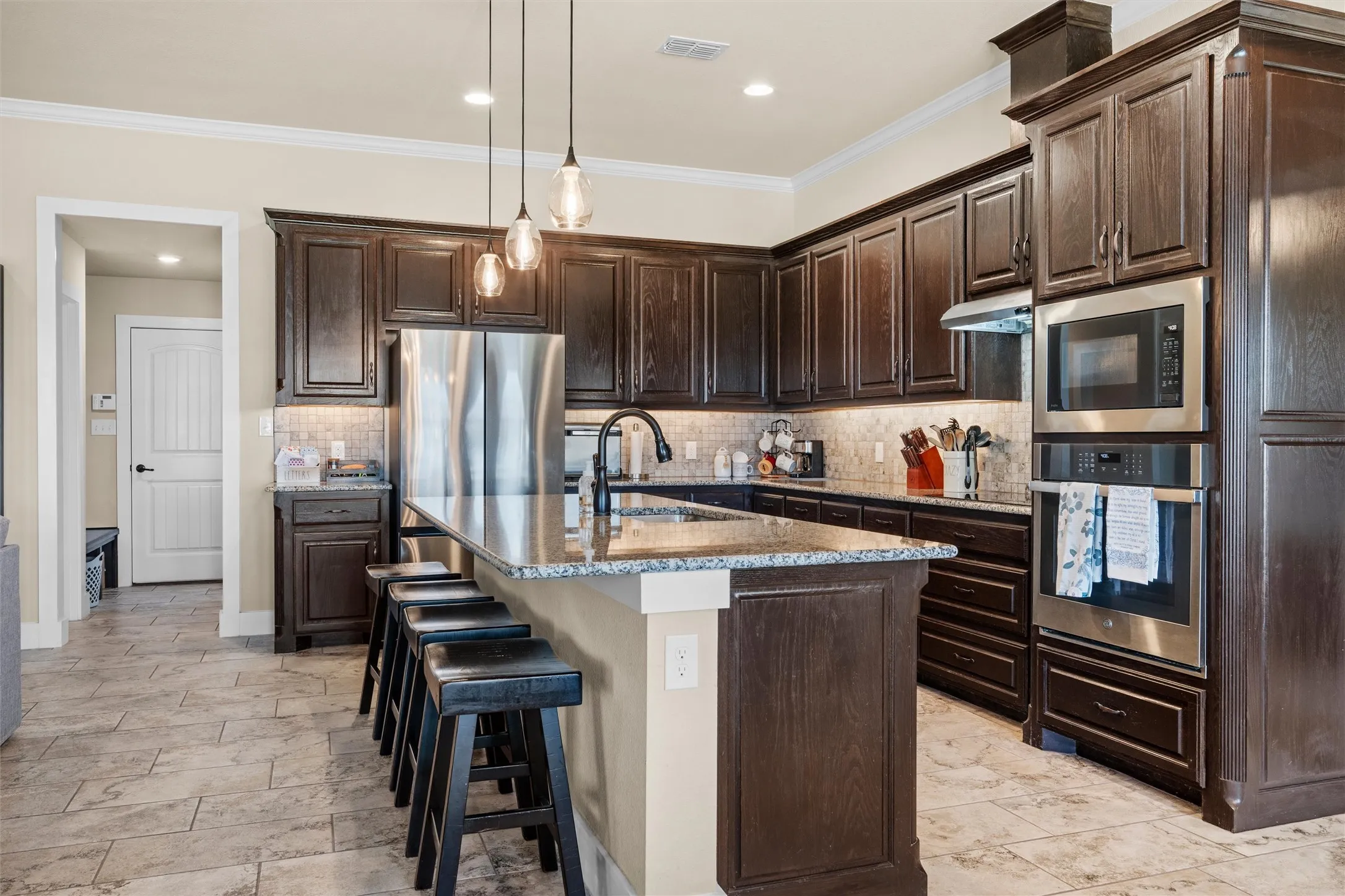 Kitchen featuring dark wood cabinetry, a large center island with seating, stainless steel appliances, and a tiled backsplash