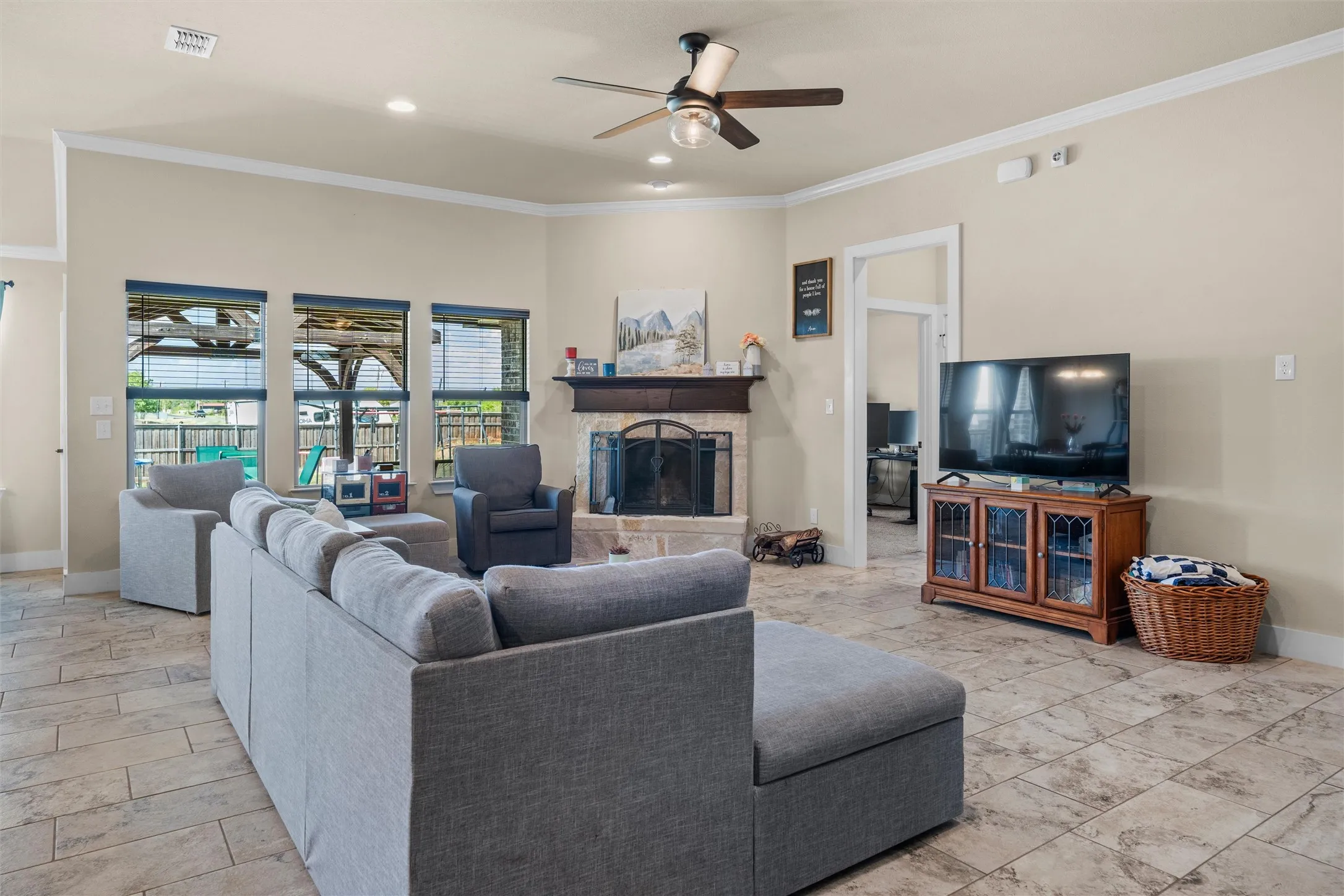 Spacious living area featuring tile flooring, a stone fireplace with wood mantel, multiple windows, and a ceiling fan with integrated lighting
