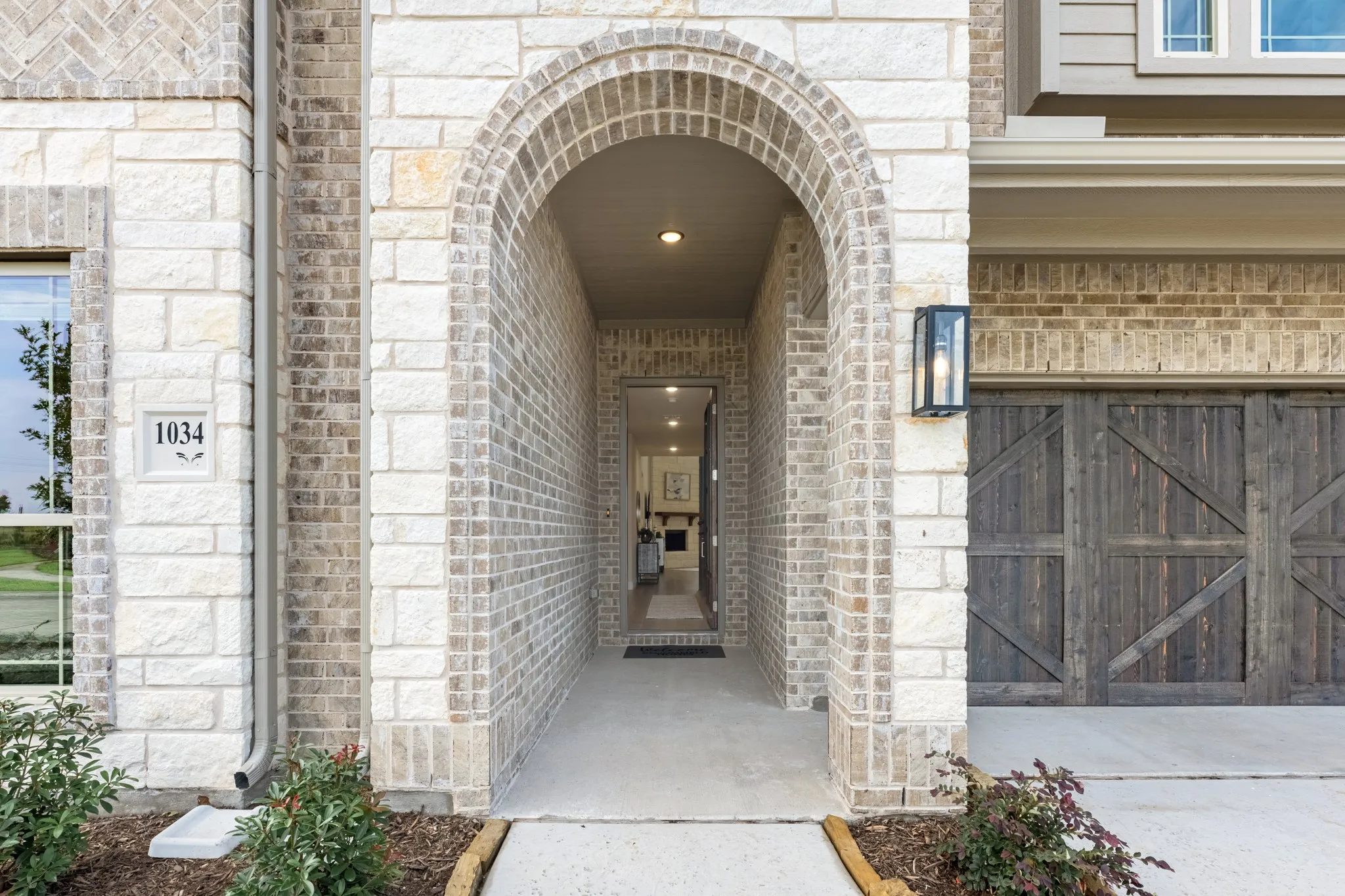Arched entryway with a brick façade, stone accents, and a coach light