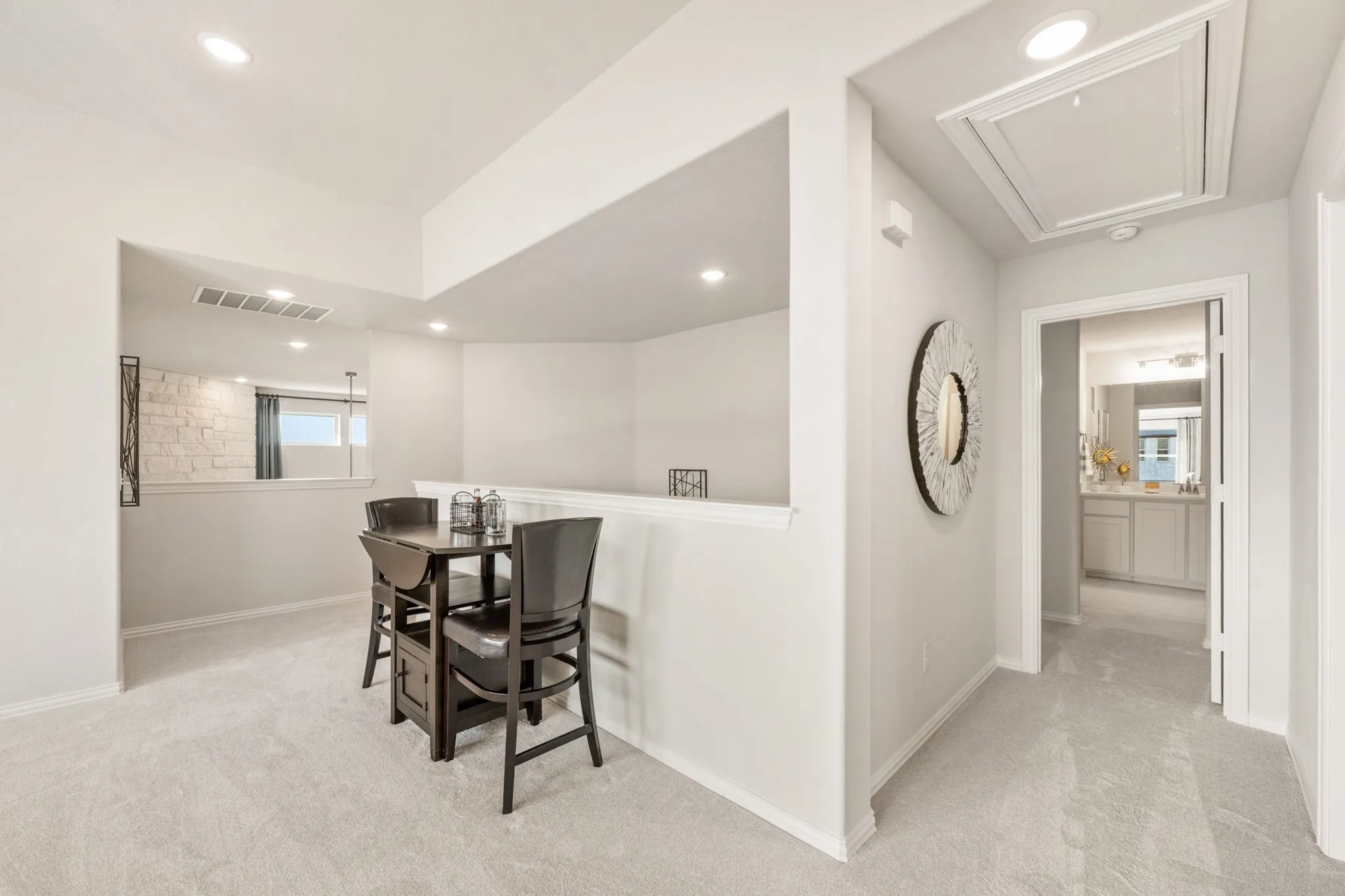 Recessed ceiling lighting, light-toned wall finishes, carpeted flooring, and an open doorway reveal a bathroom with a vanity and mirror