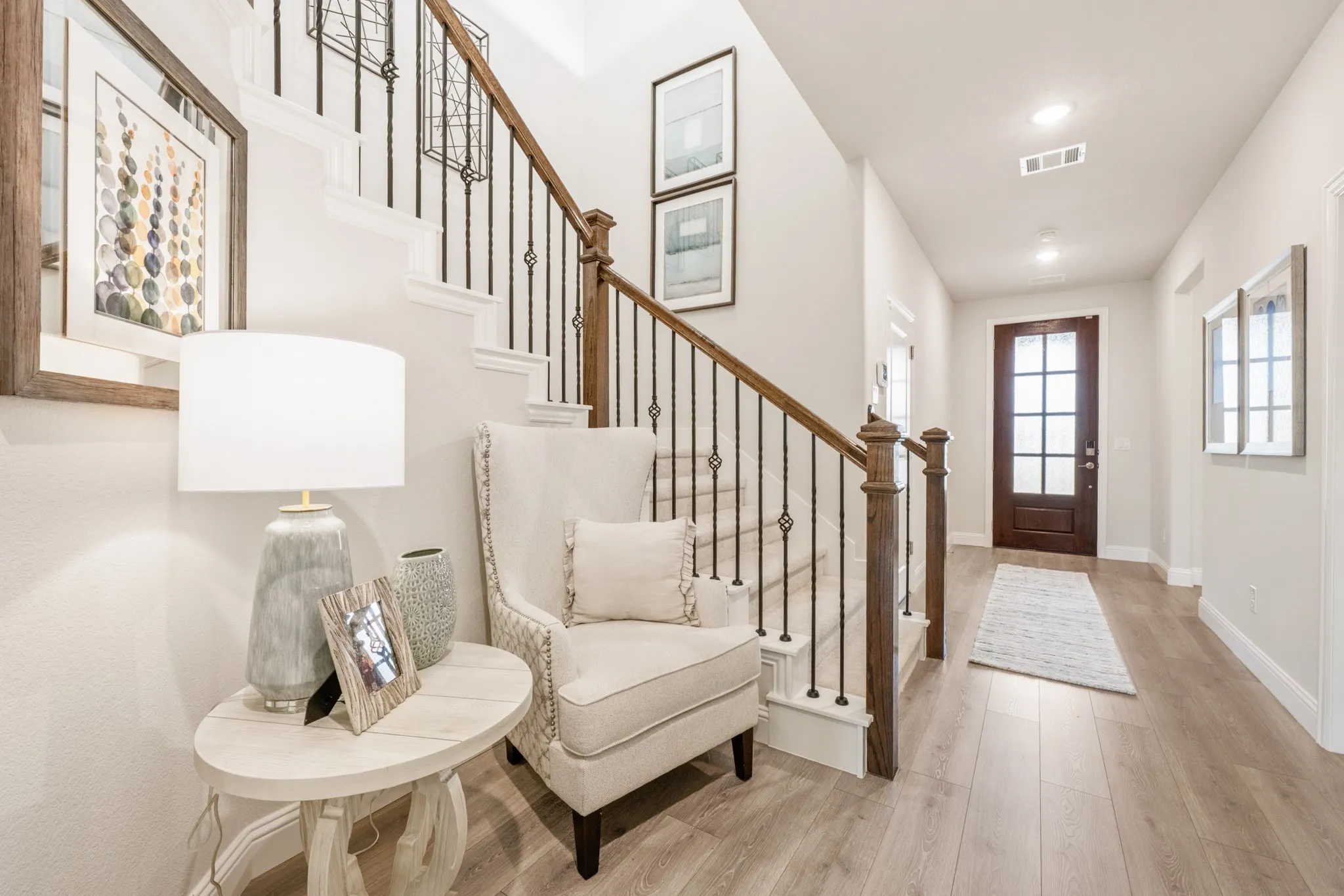 Wood-finish flooring, staircase with dark wood handrail and wrought iron balusters, recessed ceiling lights, and a glass-paneled entry door