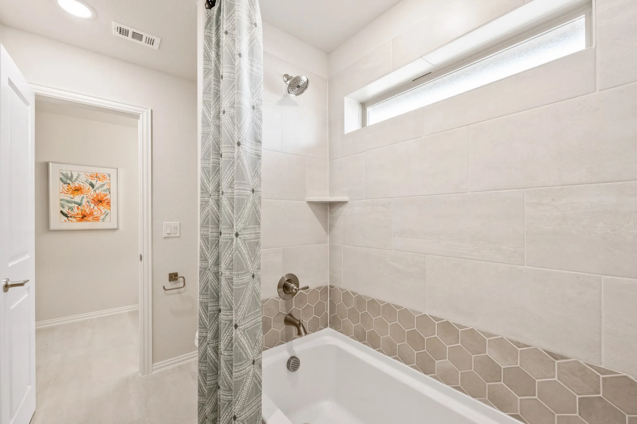 Bathtub with full-height tile surround, hexagonal accent tile, a built-in shower niche, brushed nickel fixtures, and a horizontal frosted window