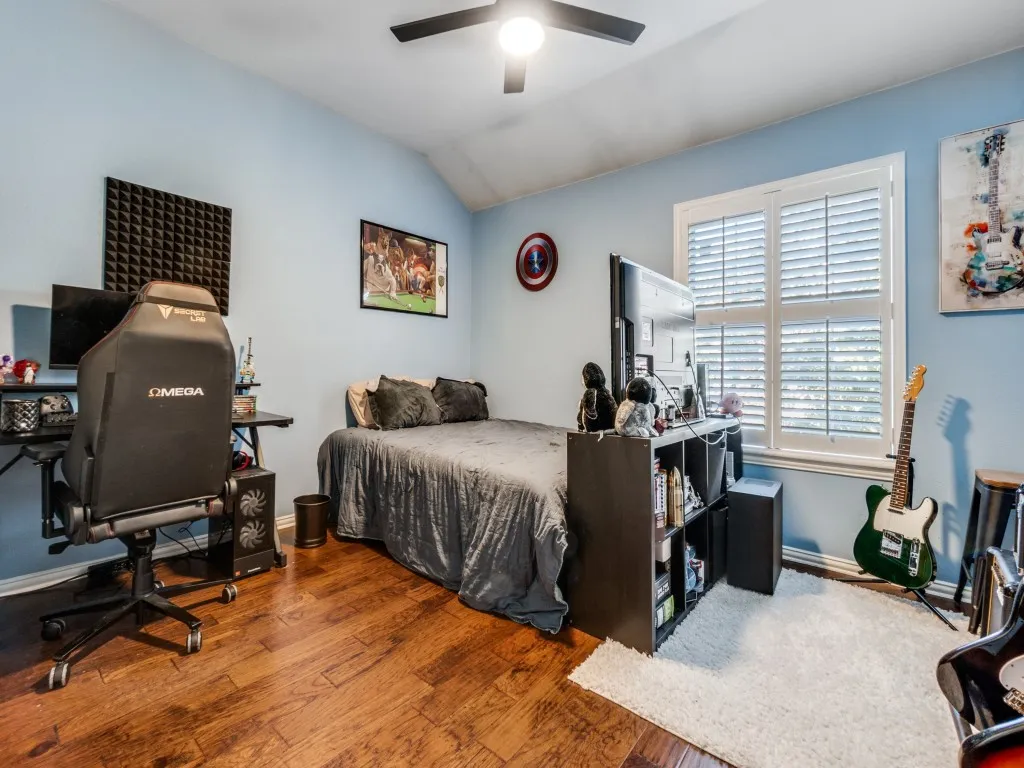 Room featuring wood-finish flooring, light blue walls, a ceiling fan, and a window with white plantation shutters