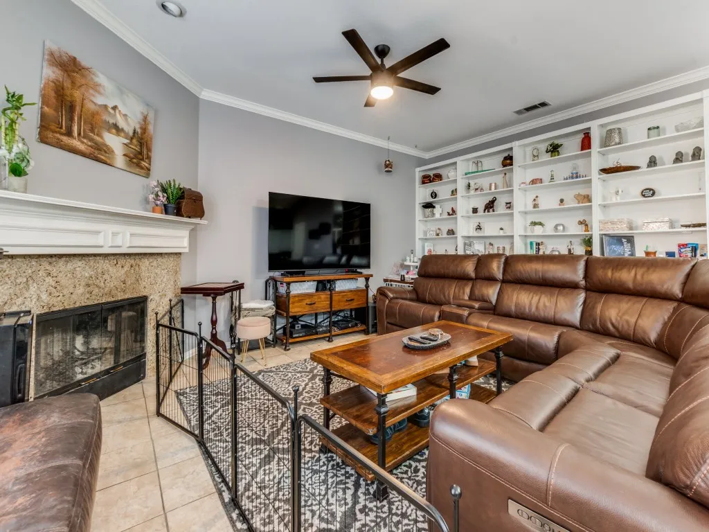 Living area featuring built-in shelving, a ceiling fan, a fireplace with a stone surround, and tile flooring