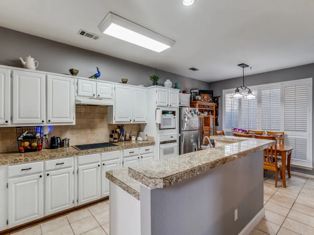 White cabinetry with dark hardware, granite countertops, tile backsplash, and stainless steel appliances