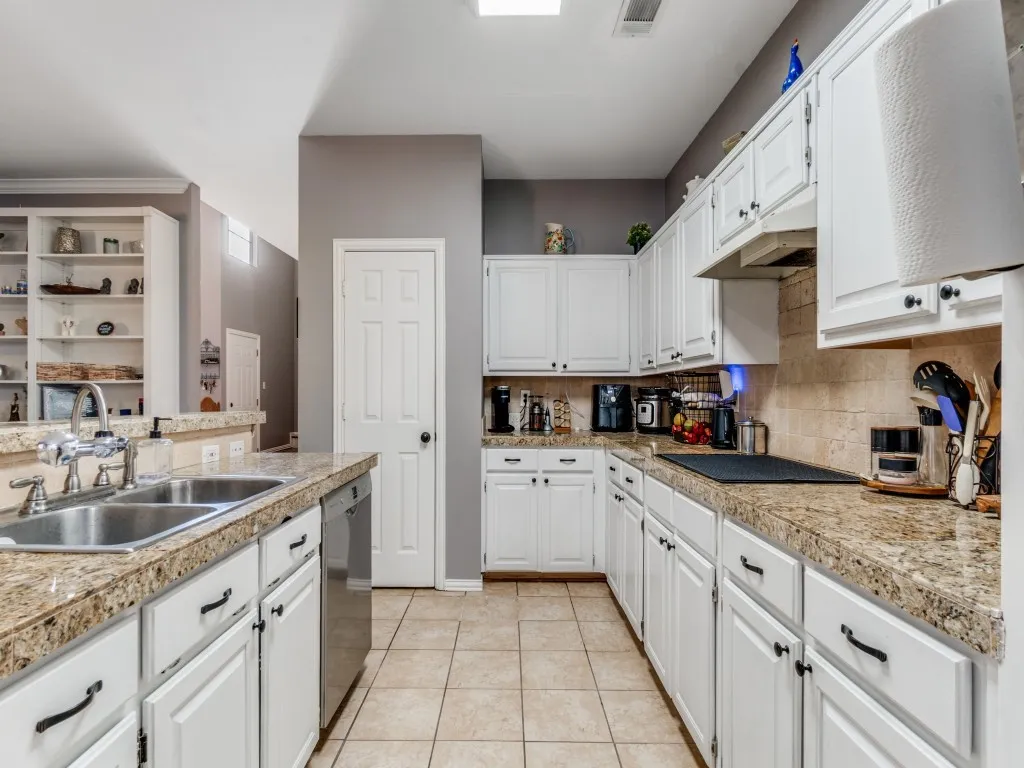 Kitchen featuring white cabinetry, stone-finish countertops, stainless steel sink, tiled flooring, and a built-in bookshelf