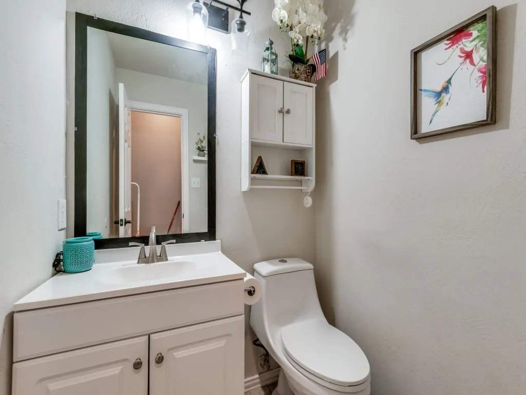 Powder bath down. White vanity with a single basin sink, framed mirror, wall-mounted light fixture, and white wall cabinet with open shelving