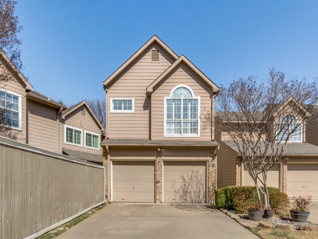 Two-story residential exterior featuring tan siding, a gabled roofline, a prominent arched window, and two ground-level garage doors