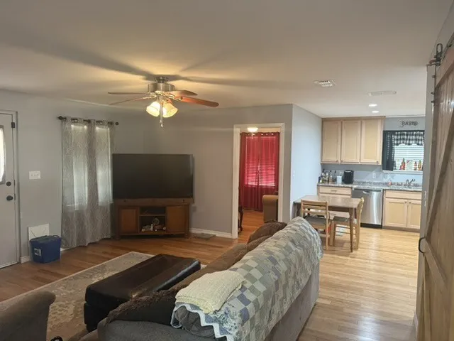 Barndominium living room. Hardwood-finish flooring, light grey wall paint, and a ceiling fan with integrated lighting.