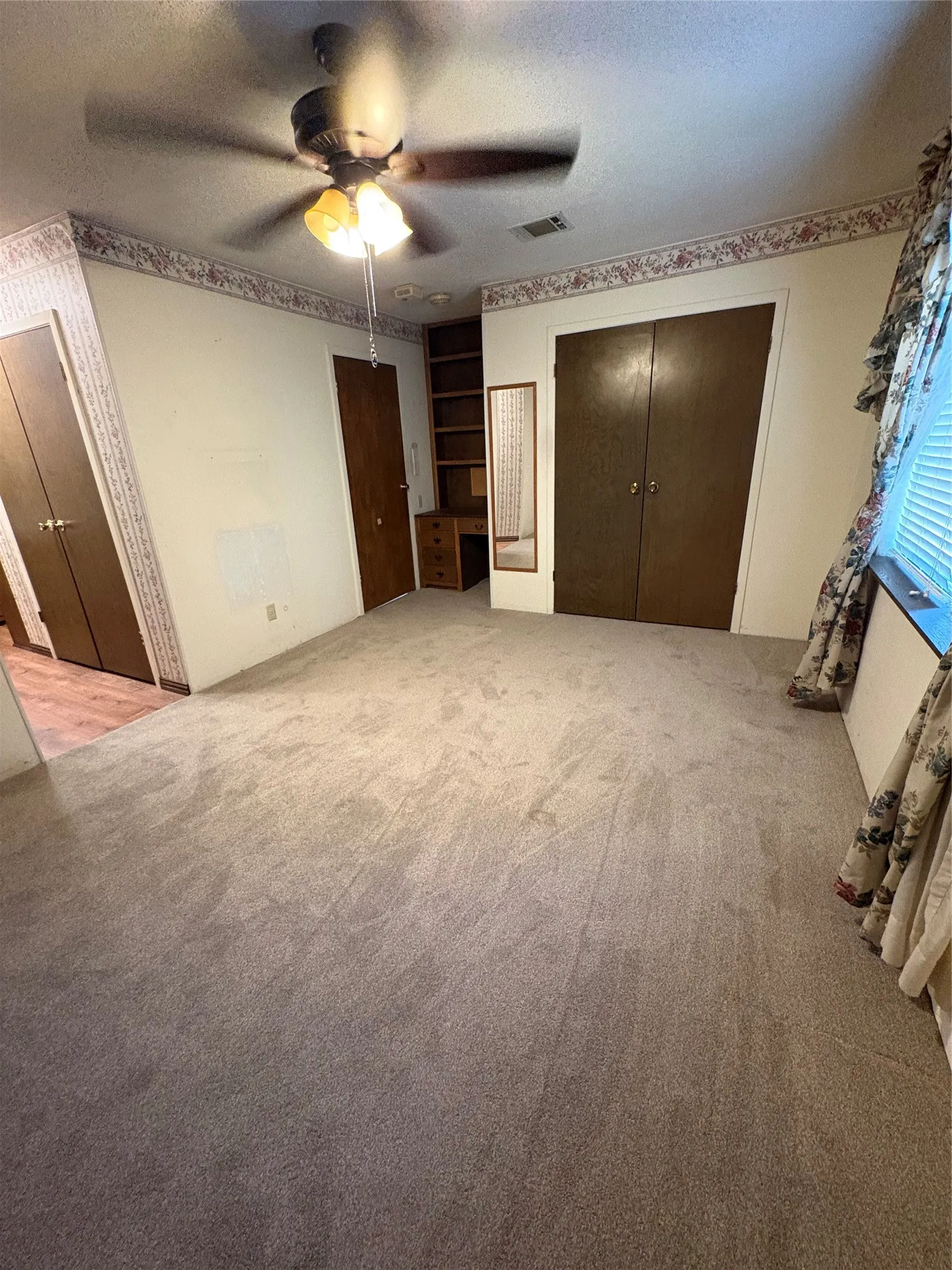 Wall-to-wall carpeting, ceiling fan with light fixture, built-in shelving, and a built-in desk