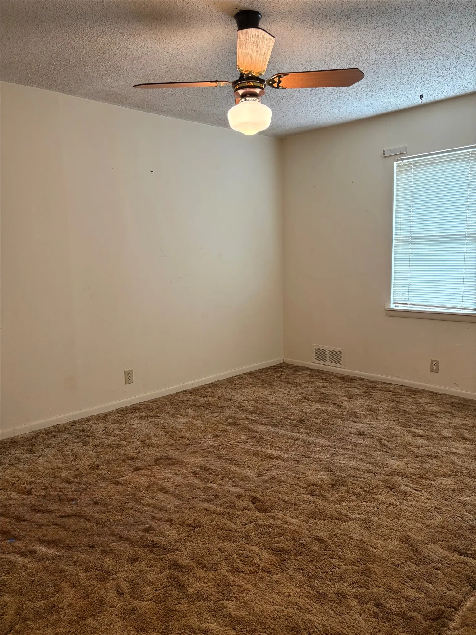 Spacious bedroom featuring neutral wall finishes, carpet flooring, a ceiling fan with integrated lighting, and abundant natural light from a large window with blinds.
